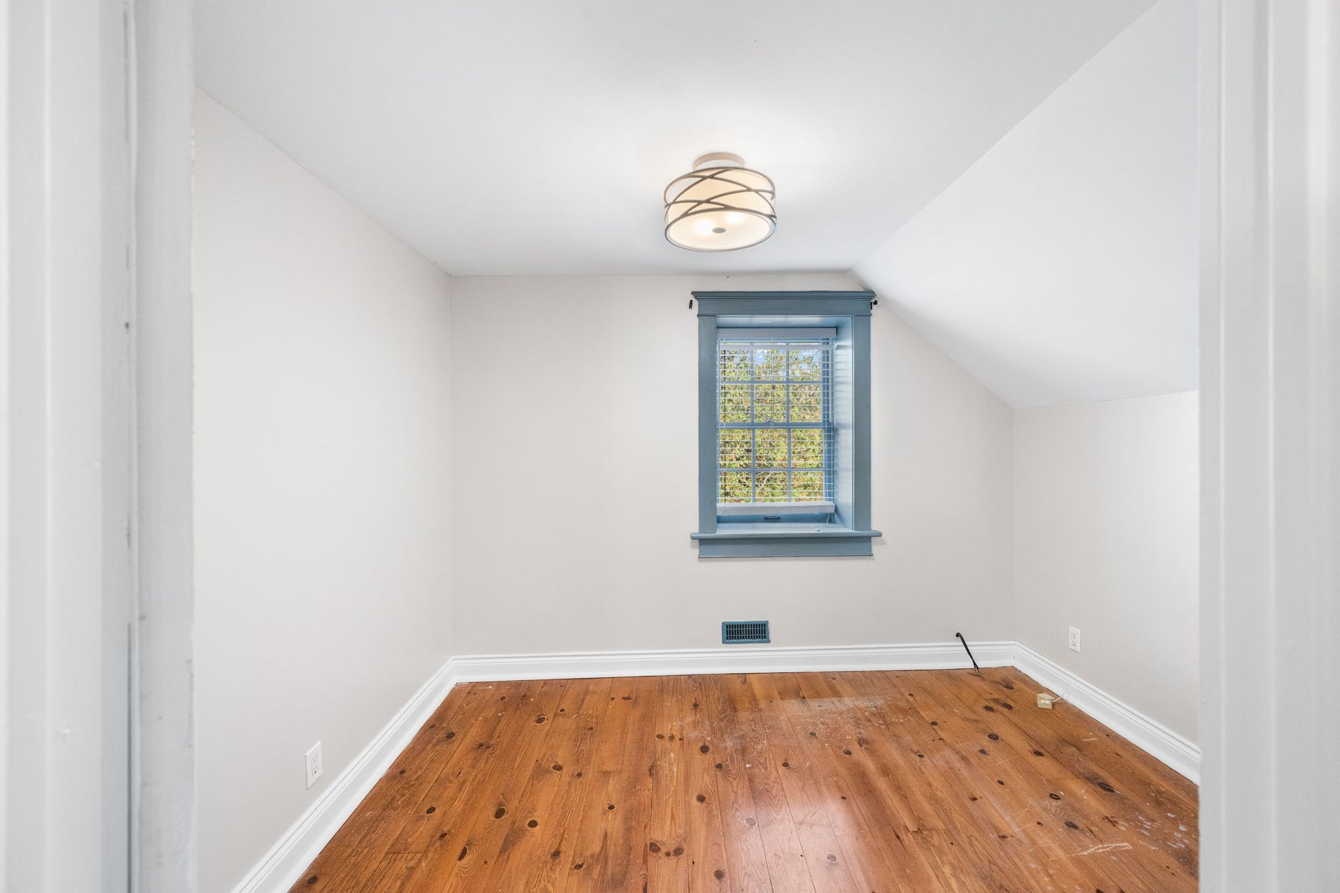 Empty room with hardwood floors, a small window with blue trim, and a ceiling light.