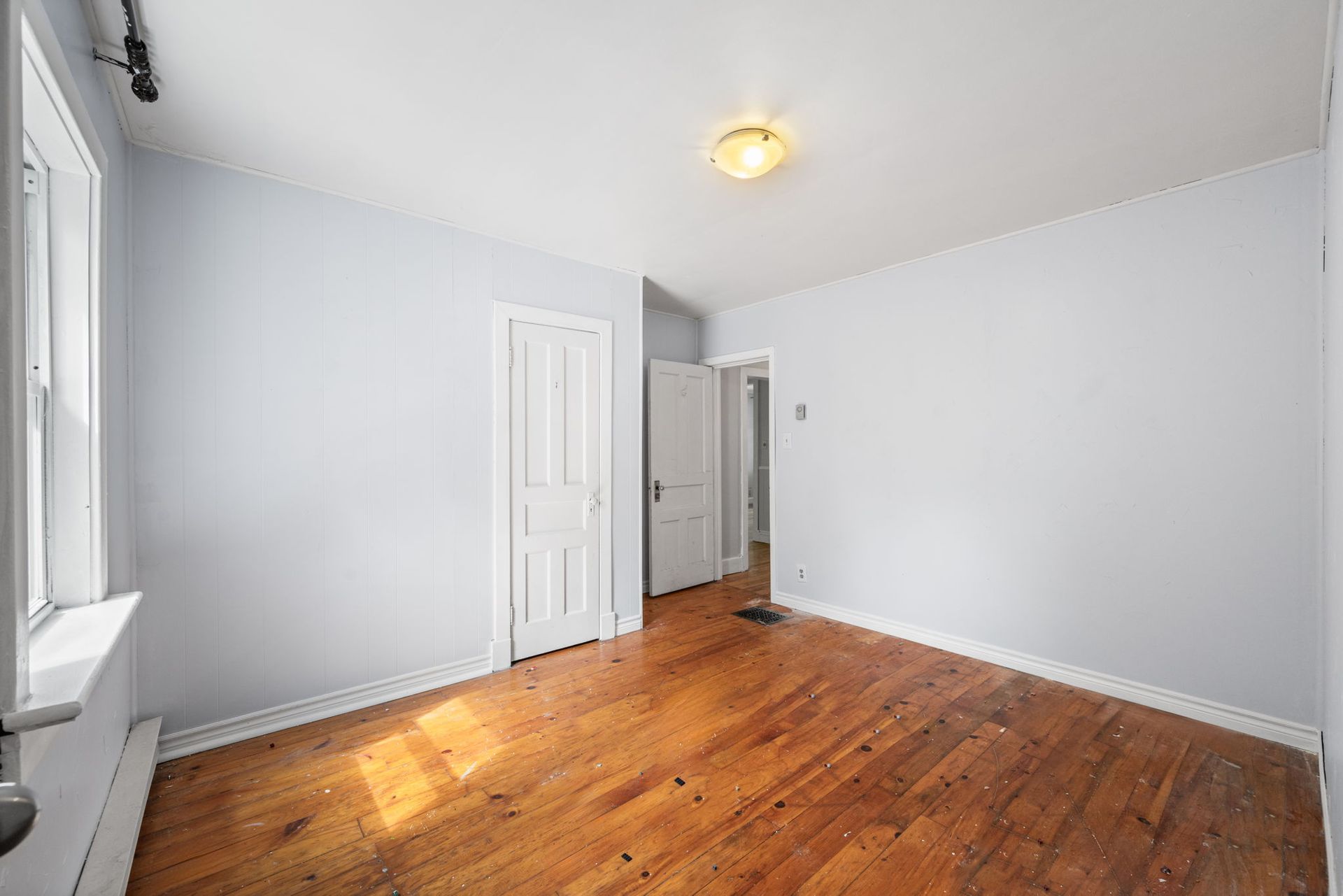 Empty room with wood floor, light blue walls, and a white door.