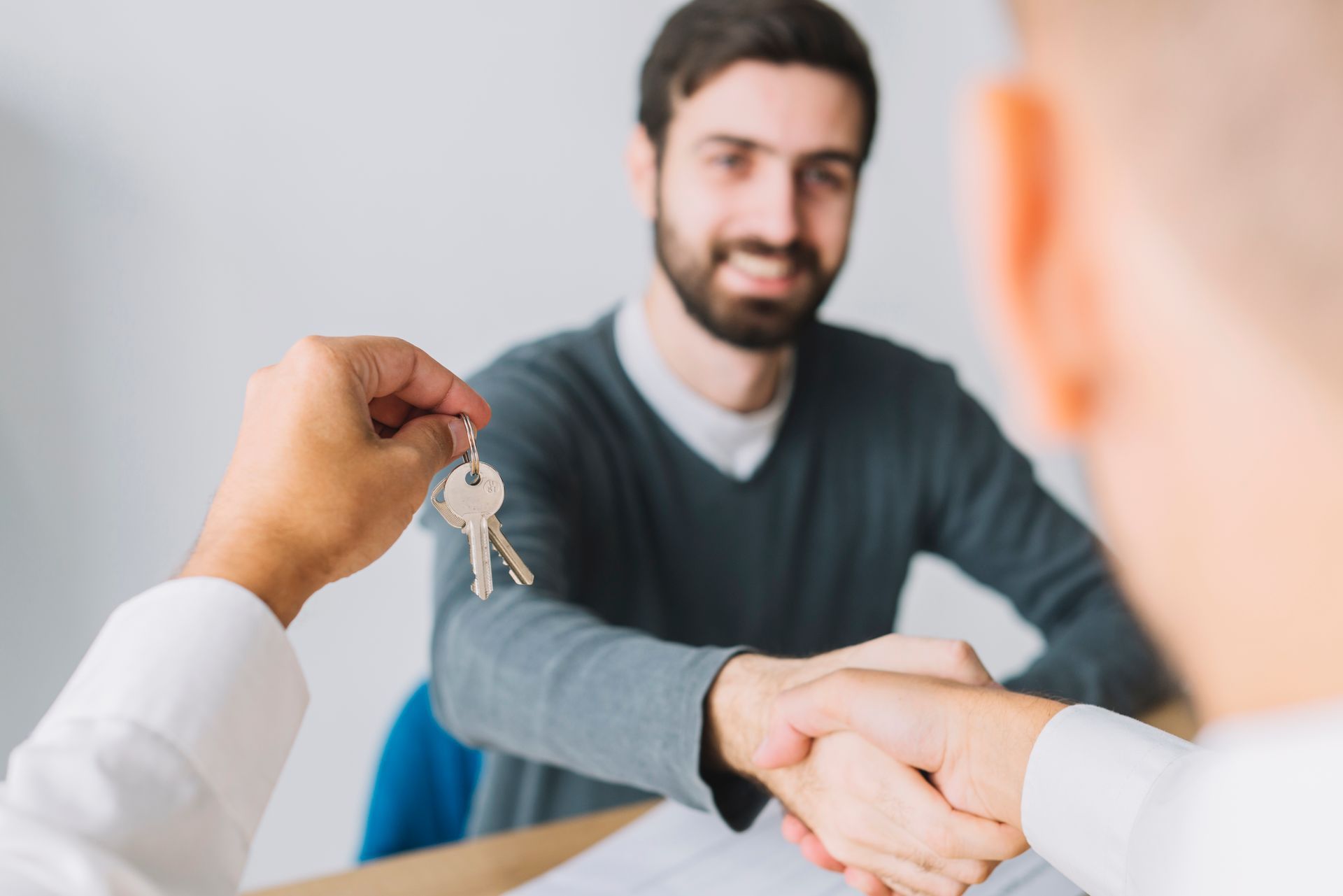 A man is shaking hands with another man while holding a key.