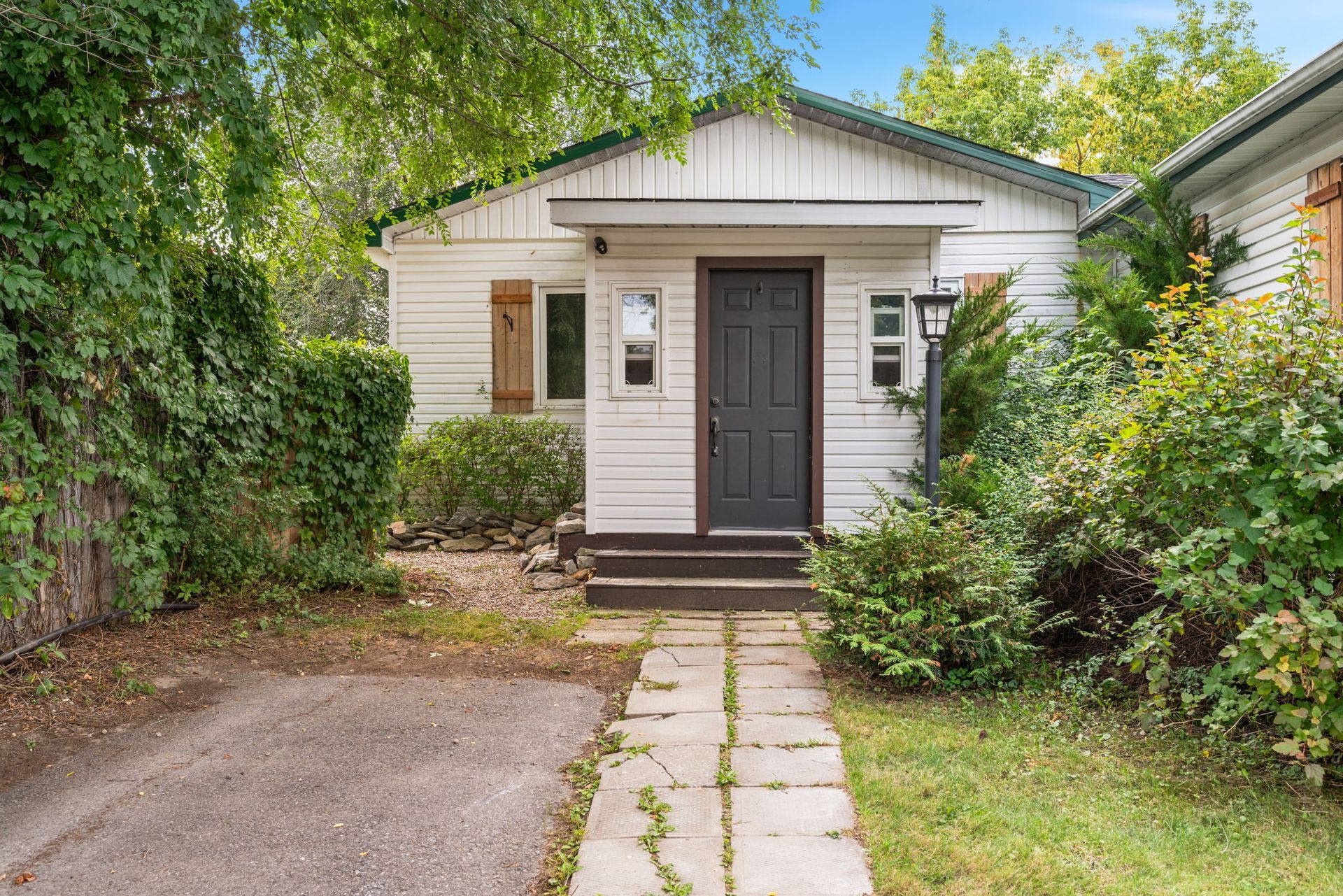 White cottage with dark door, stone path, surrounded by greenery and shrubs.
