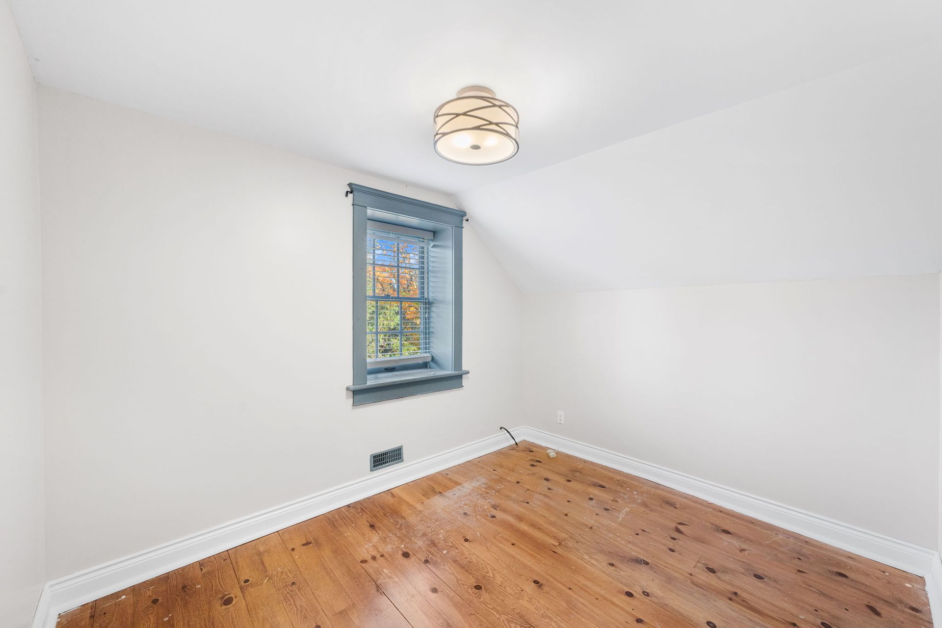 Empty room with hardwood floors, a small window, and a ceiling light. White walls and blue window trim.
