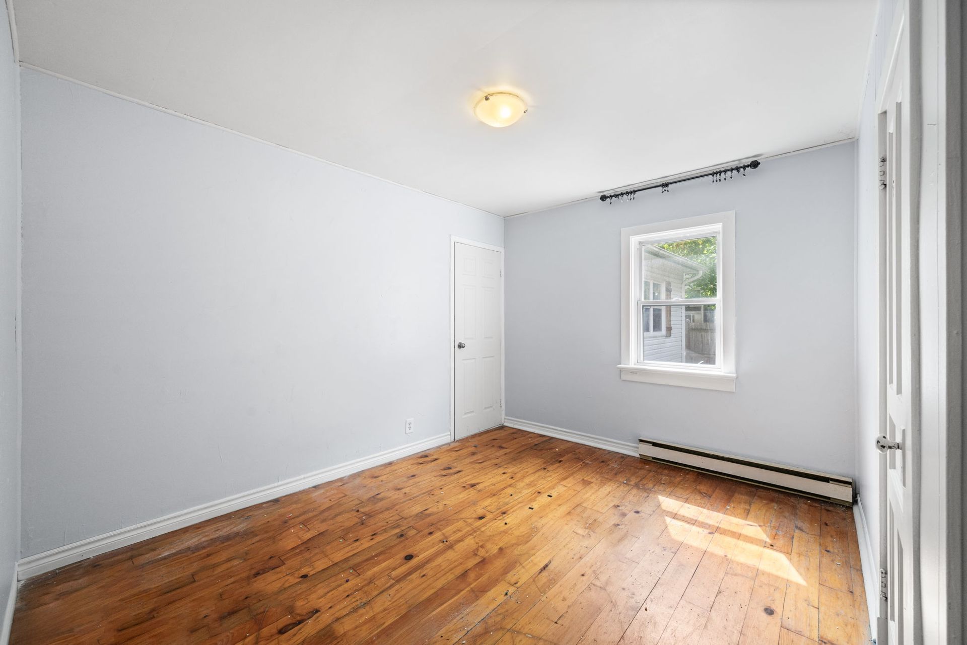 Empty room with light blue walls, wood floors, and a window.