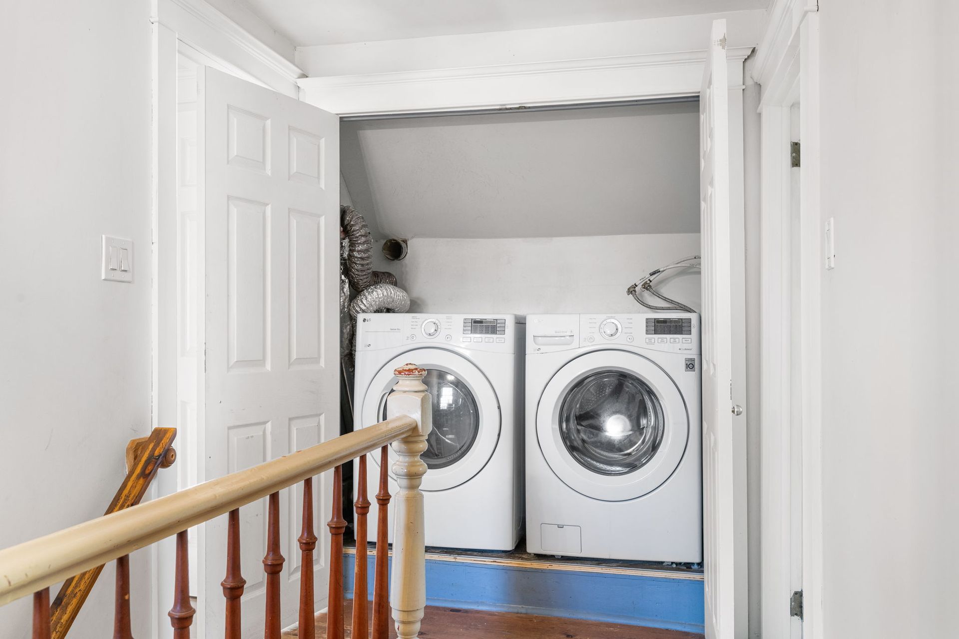Laundry machines in a small alcove with a door and a wooden railing.