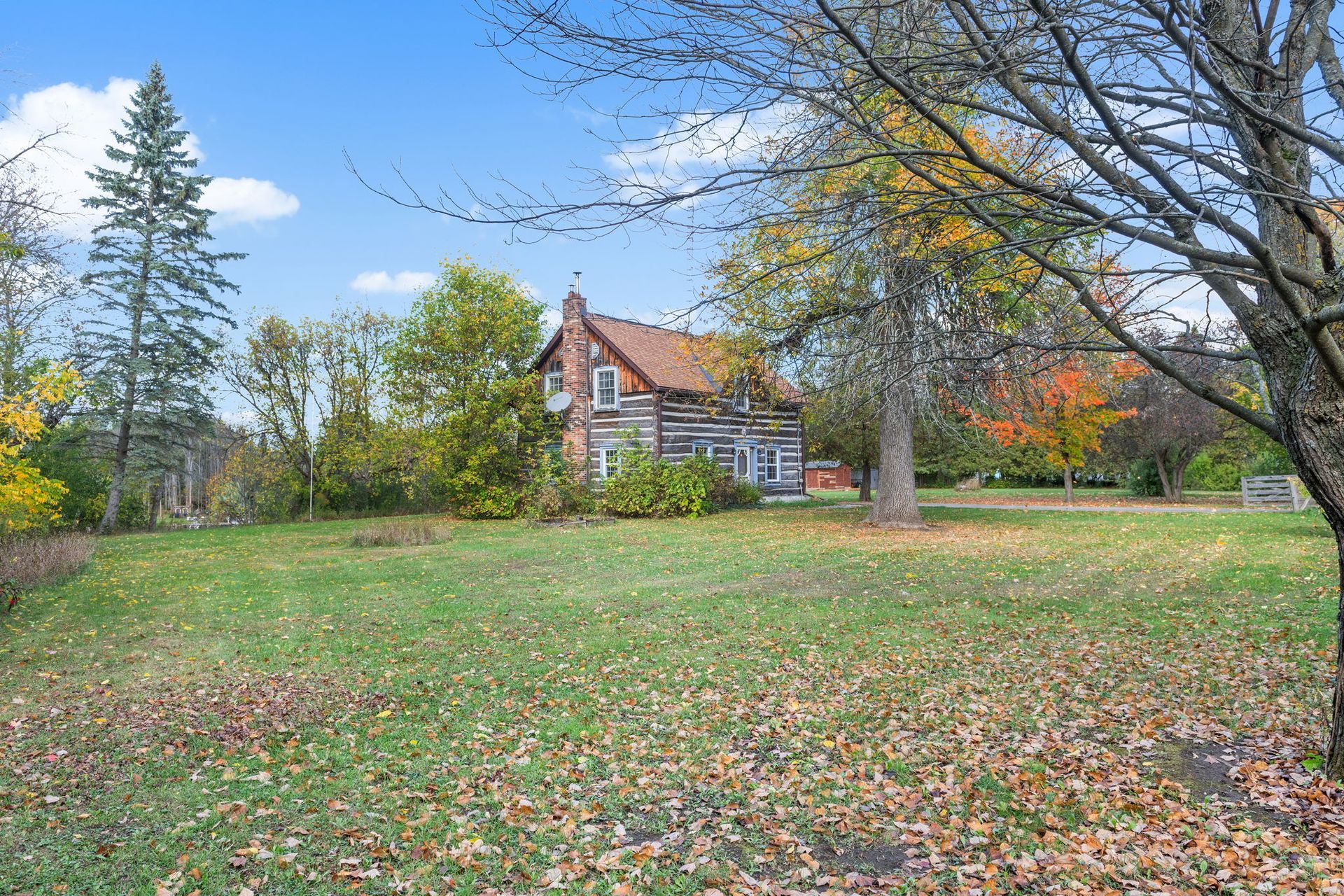 Log cabin in a grassy yard, surrounded by trees with autumn leaves.