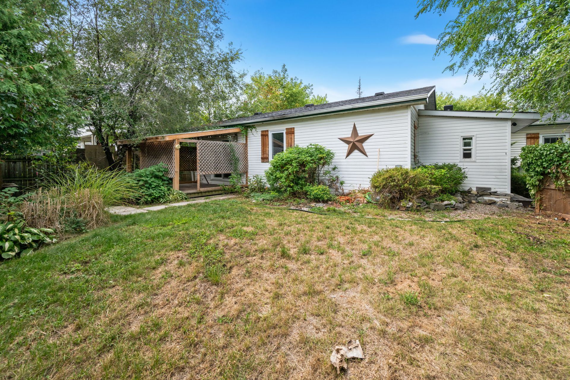 White house with wooden porch and star decoration on the side. Lush green yard.