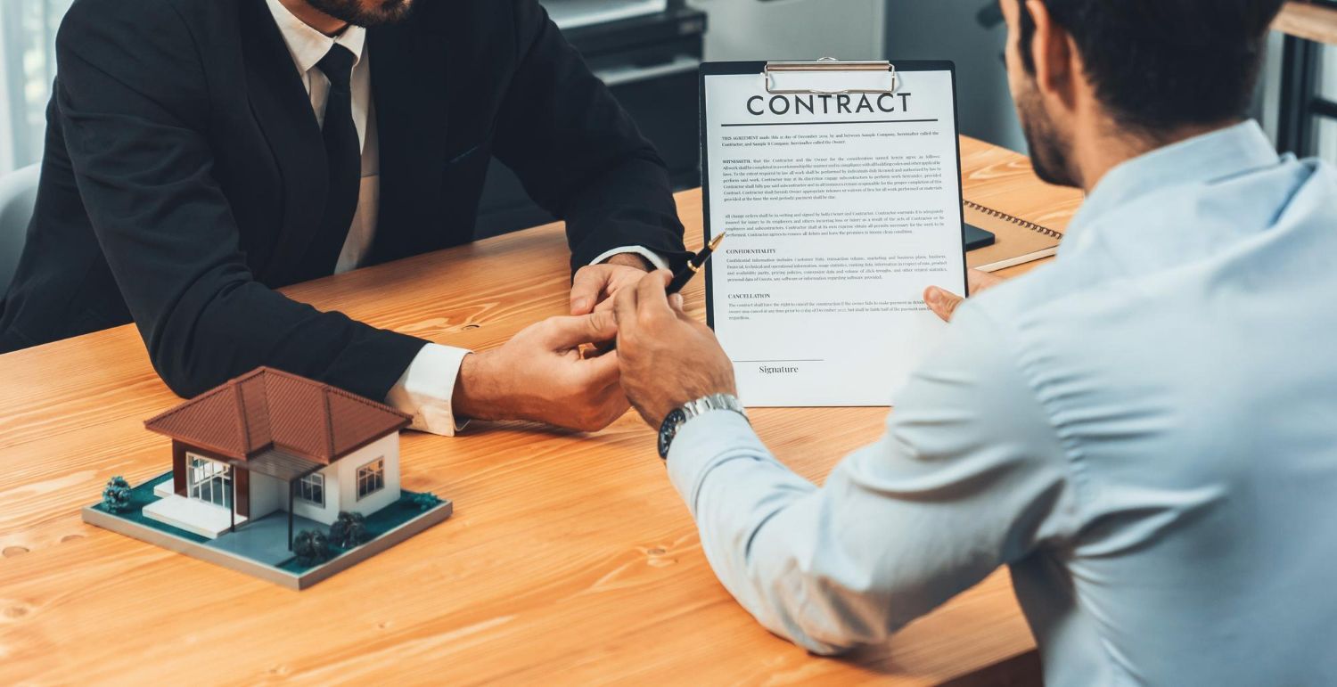 A man is sitting at a table signing a contract with another man.