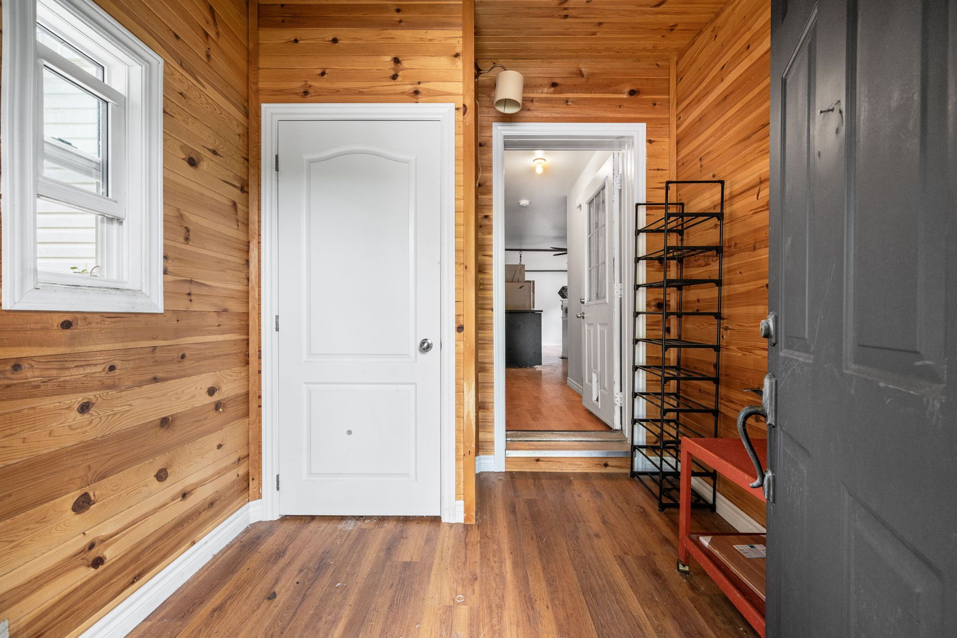 Wooden entryway with white doors, window, and black shoe rack.