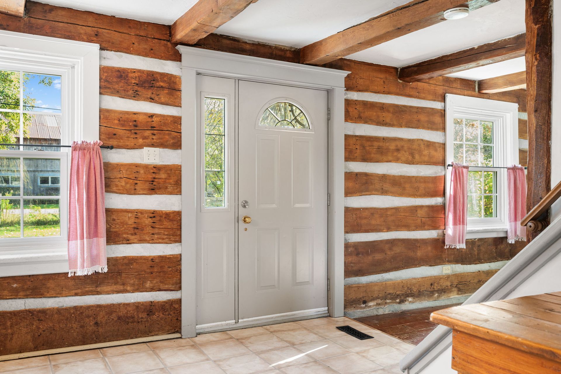 Interior view of a log cabin with a front door, windows, and exposed beams.