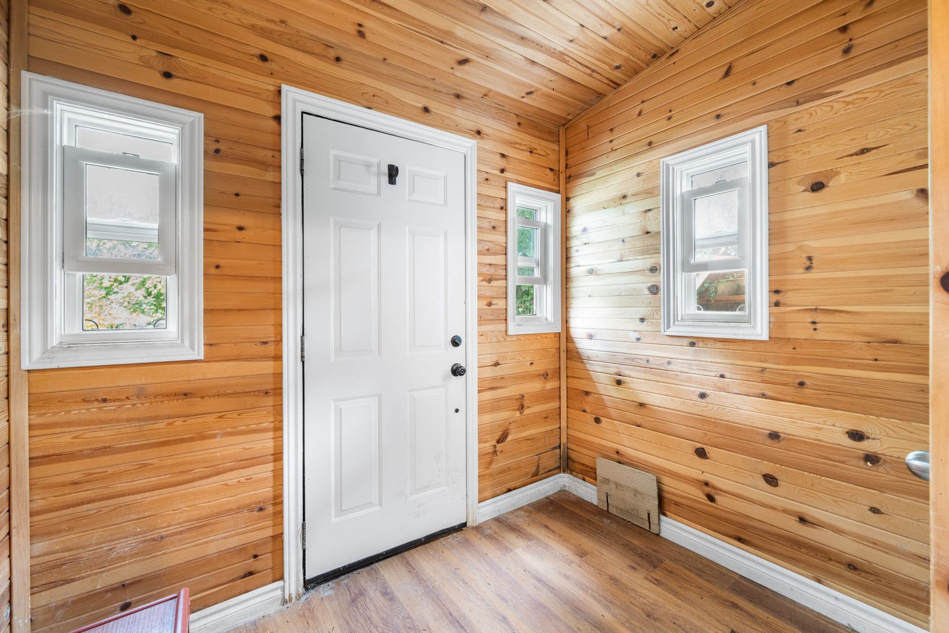 Wooden-walled entryway with white door and windows; natural wood flooring and trim.
