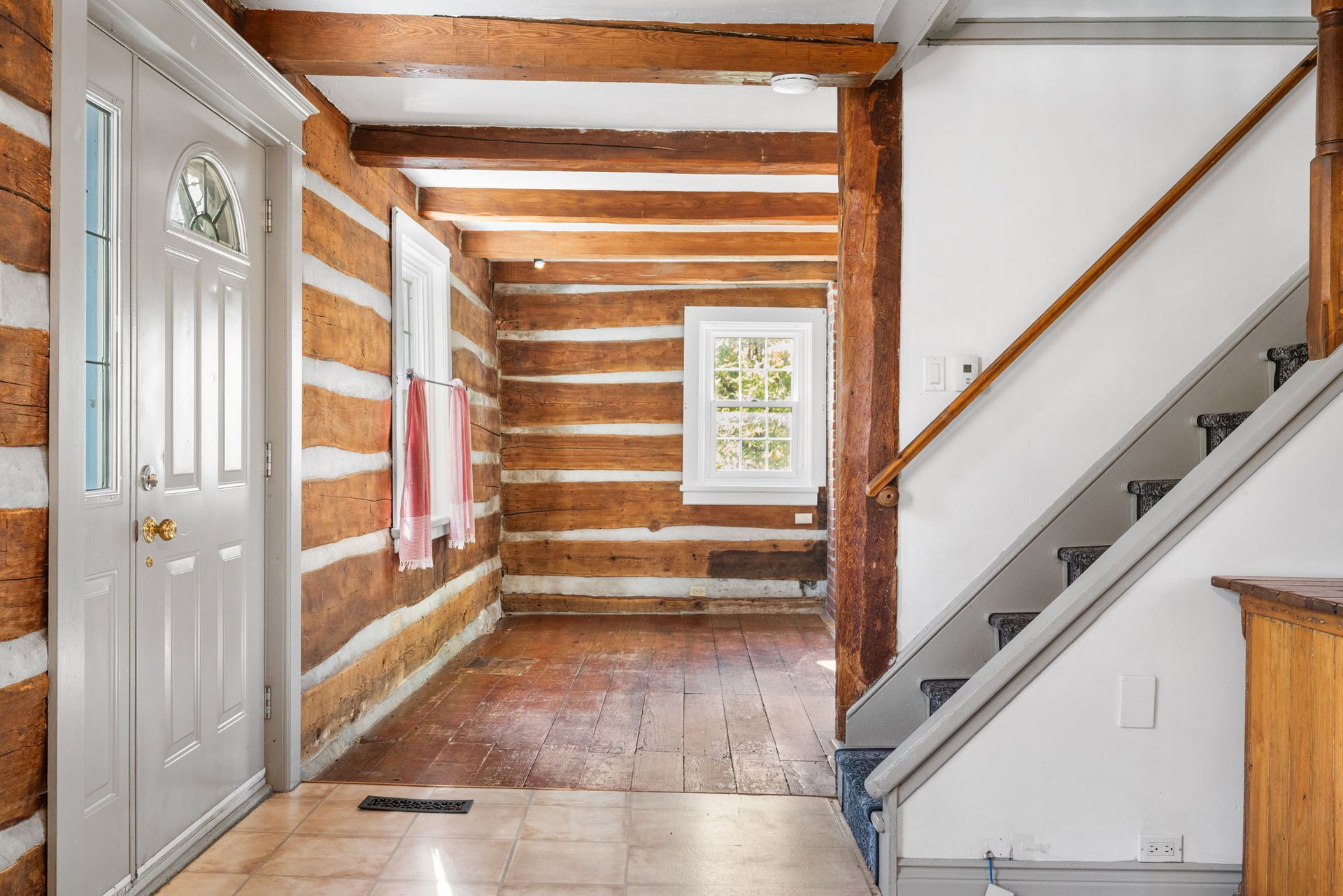 Interior hallway with log walls, wood floors, staircase, and white door.