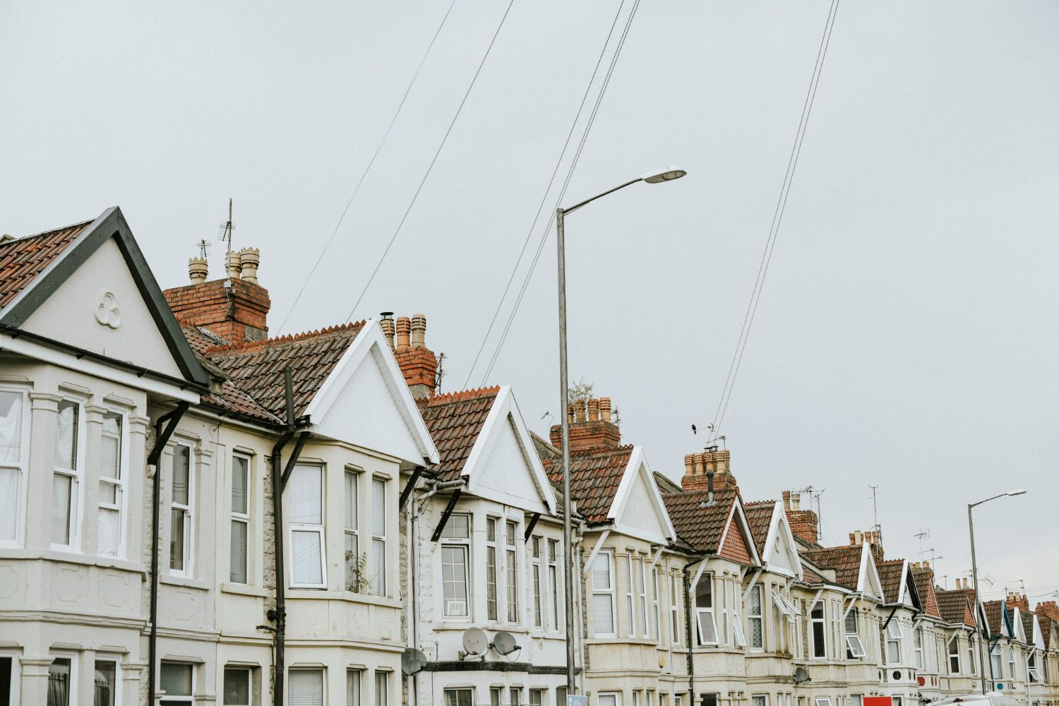 A row of houses with chimneys on the roofs are lined up on a street.