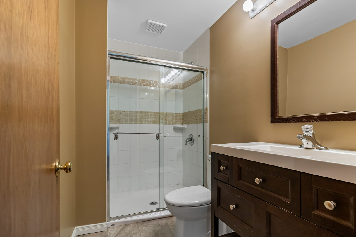 Bathroom with a brown vanity, glass shower, and beige walls.
