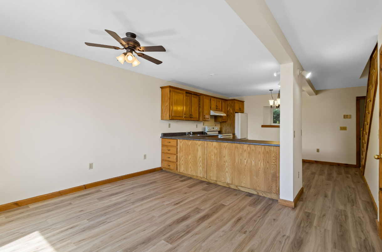 Open-concept living space with kitchen. Oak cabinets, light wood flooring, beige walls, ceiling fan.