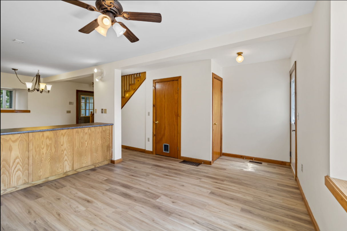 Bright interior room with wood flooring, ceiling fan, and doors leading to other rooms.