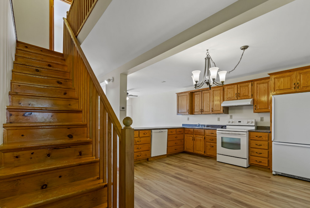Wooden staircase next to kitchen with oak cabinets, white appliances, and chandelier.