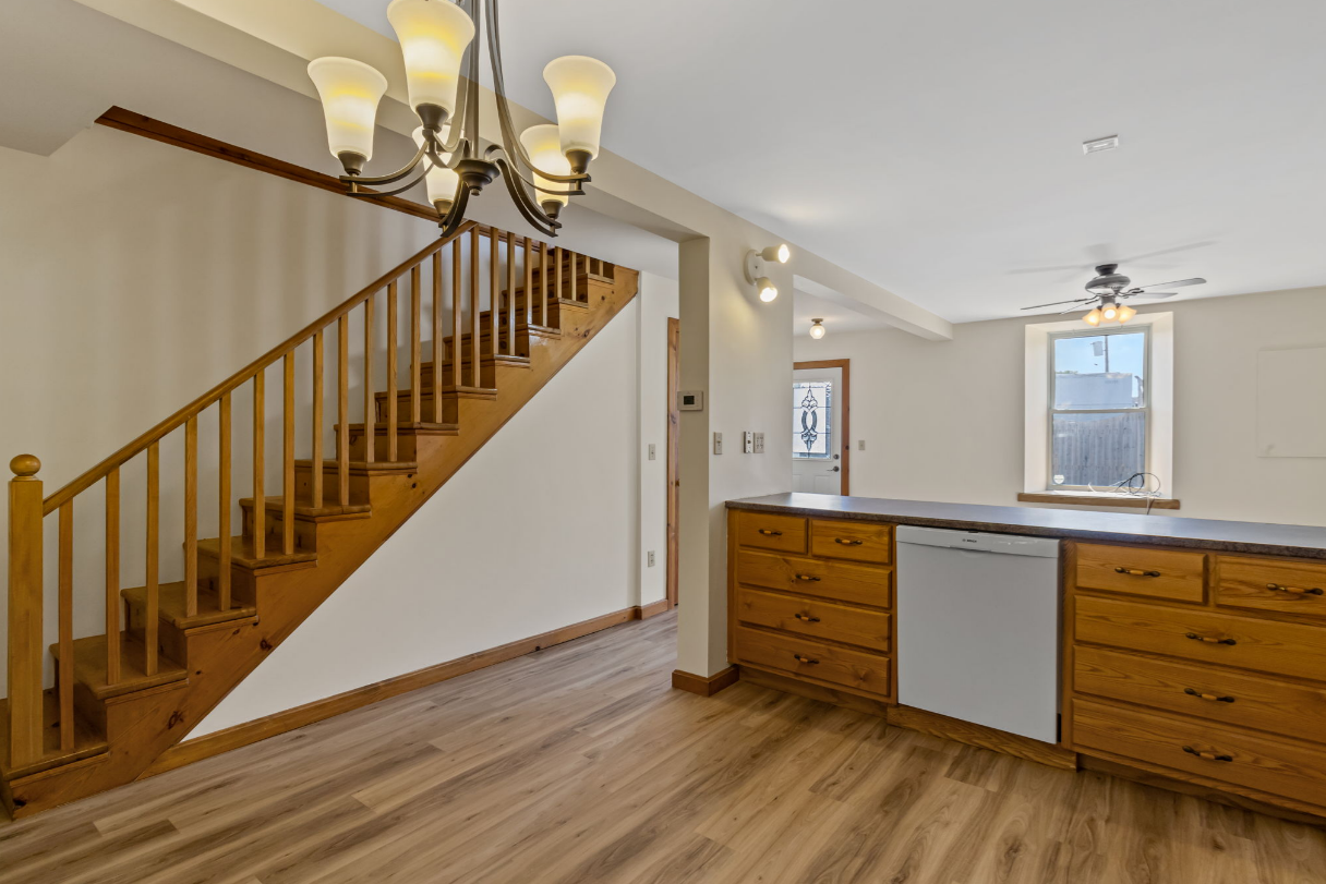 Interior of a home with a wooden staircase, kitchen cabinets, and a chandelier.
