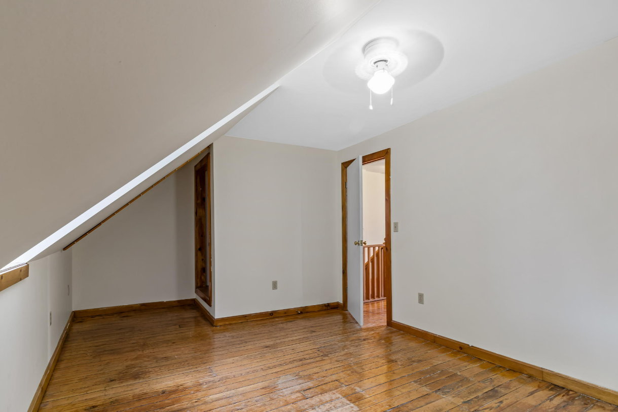 Empty room with slanted ceiling, hardwood floor, and doorway.