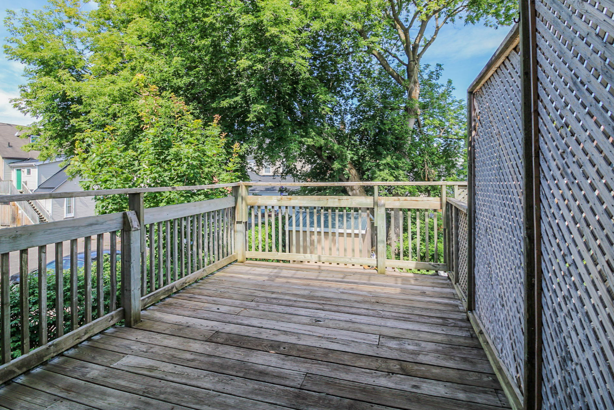 Wooden deck with railing, lattice screen, and view of trees and buildings.