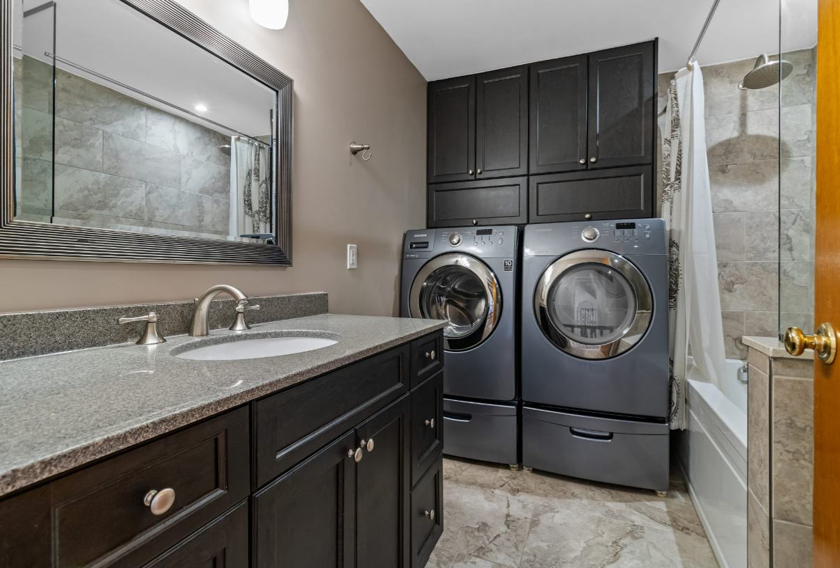 Bathroom with dark cabinets, a washer and dryer, and a granite countertop.