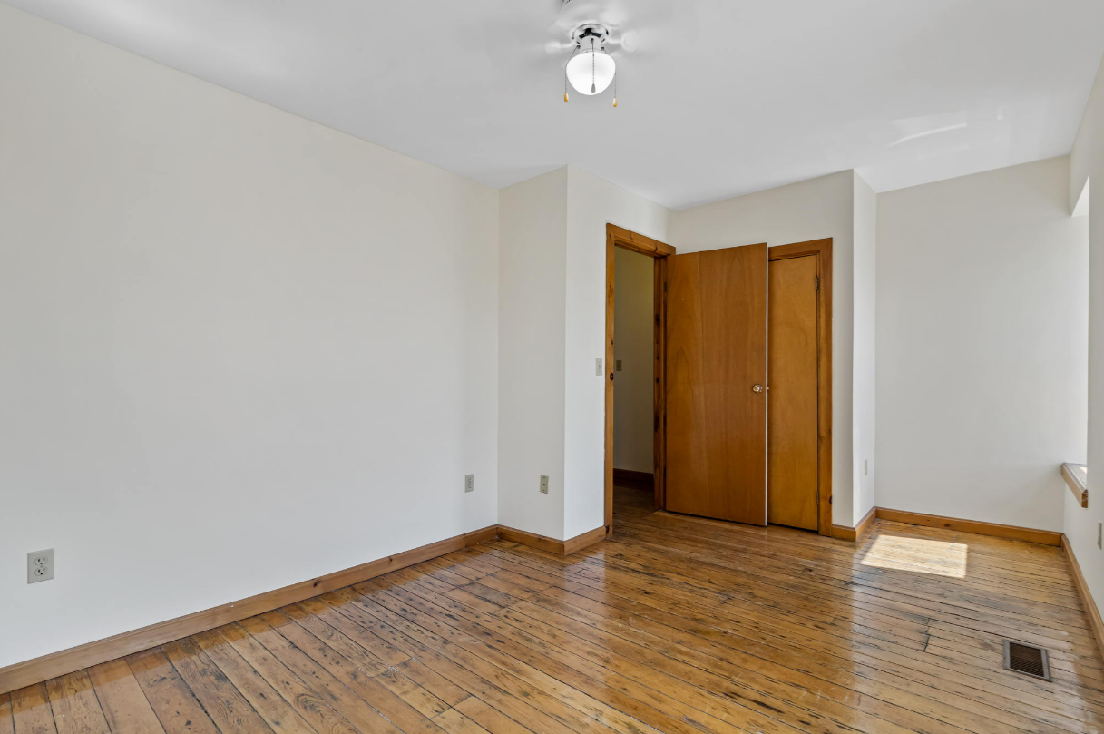 Empty room with hardwood floors, white walls, closet, and a light fixture.