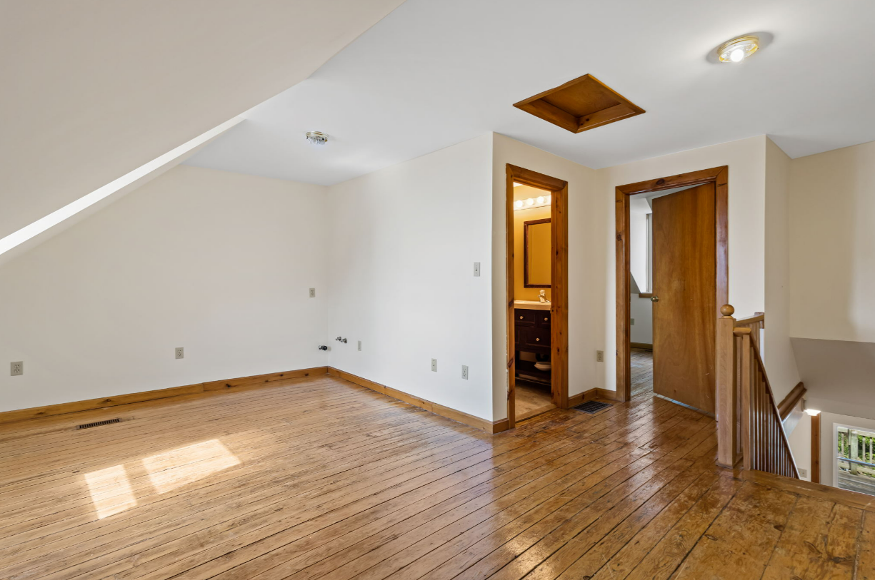 Empty room with wooden floor, sloped wall, and doorways to bathroom and other room.