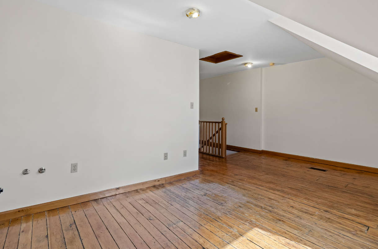 Empty room with hardwood floors, white walls, and a small stairwell visible.