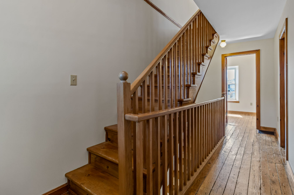 Wooden staircase with railing in a hallway with wood flooring.