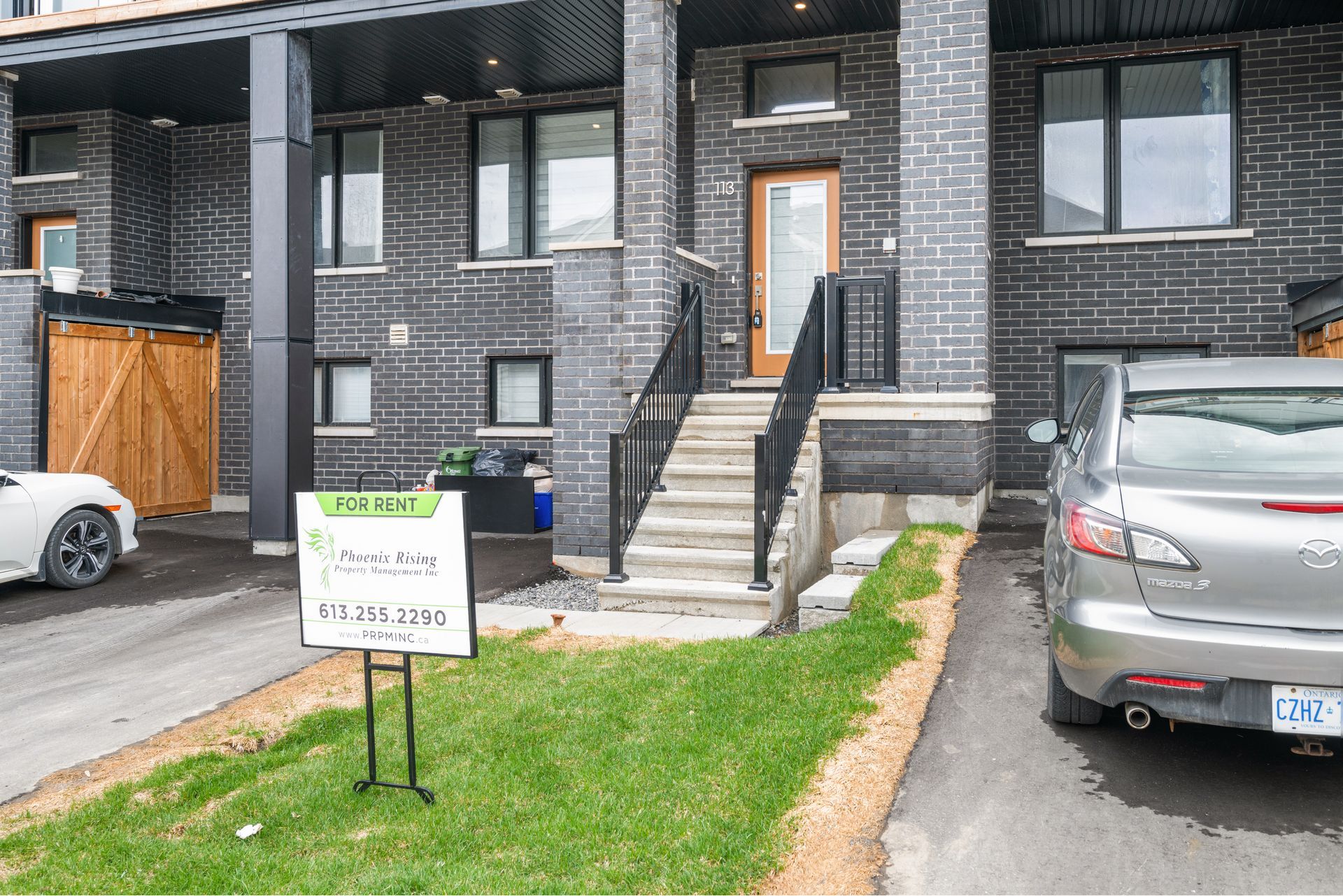 A car is parked in front of a house with a for sale sign.