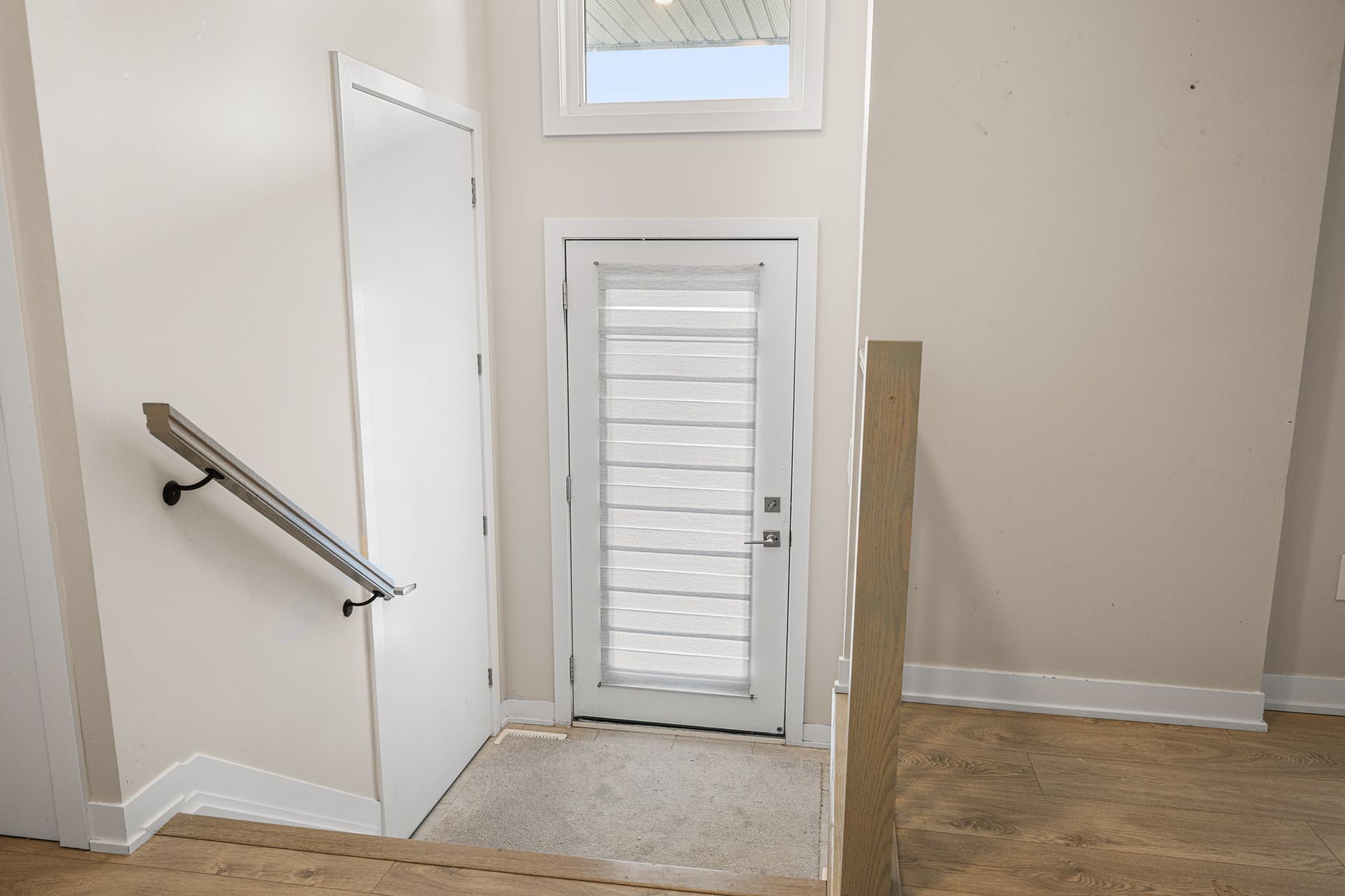 A hallway with stairs leading up to a door and a window.