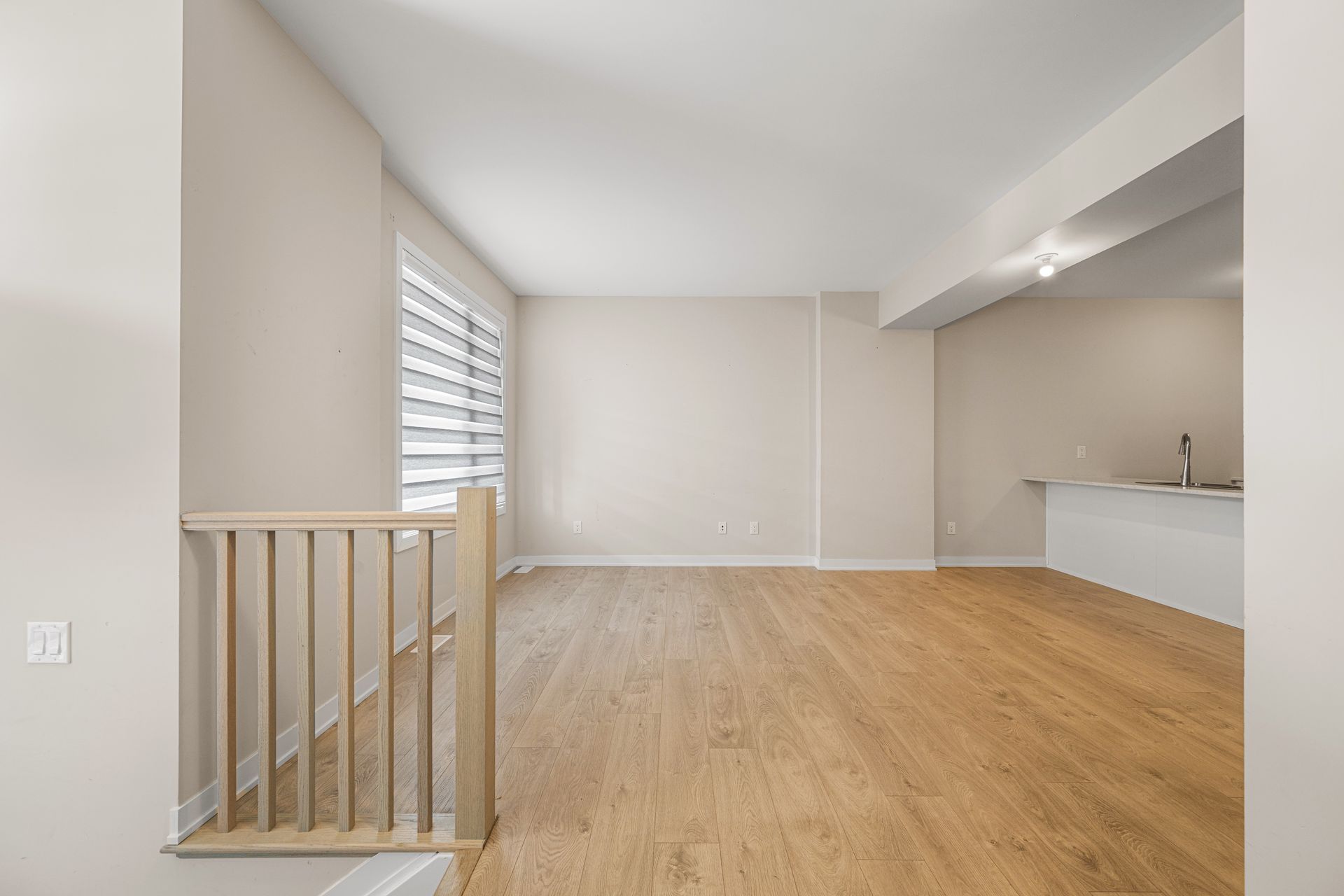 An empty living room with hardwood floors and stairs leading to a kitchen.