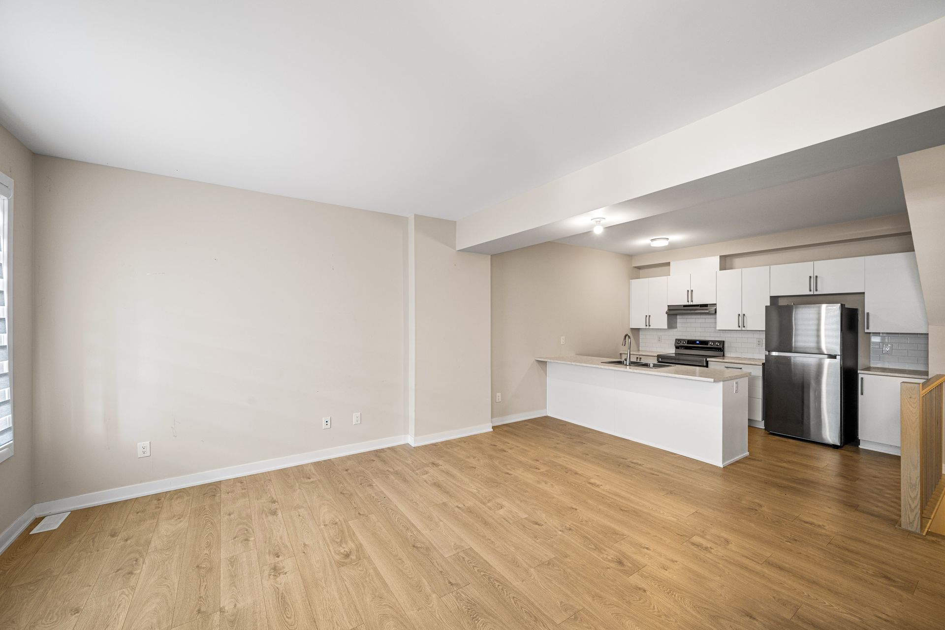 An empty living room with hardwood floors and a kitchen in the background.