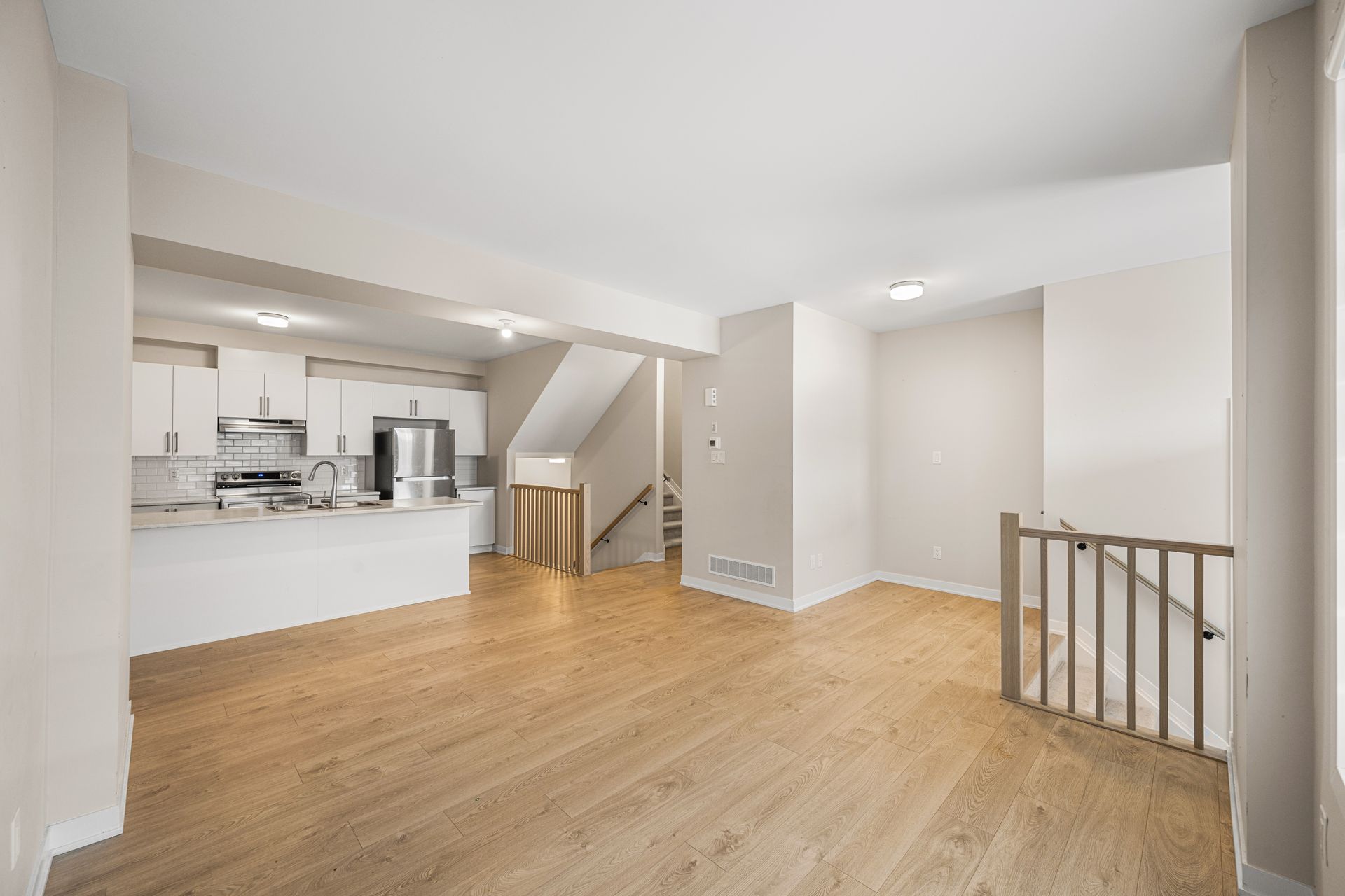 A living room with hardwood floors and a kitchen in the background.
