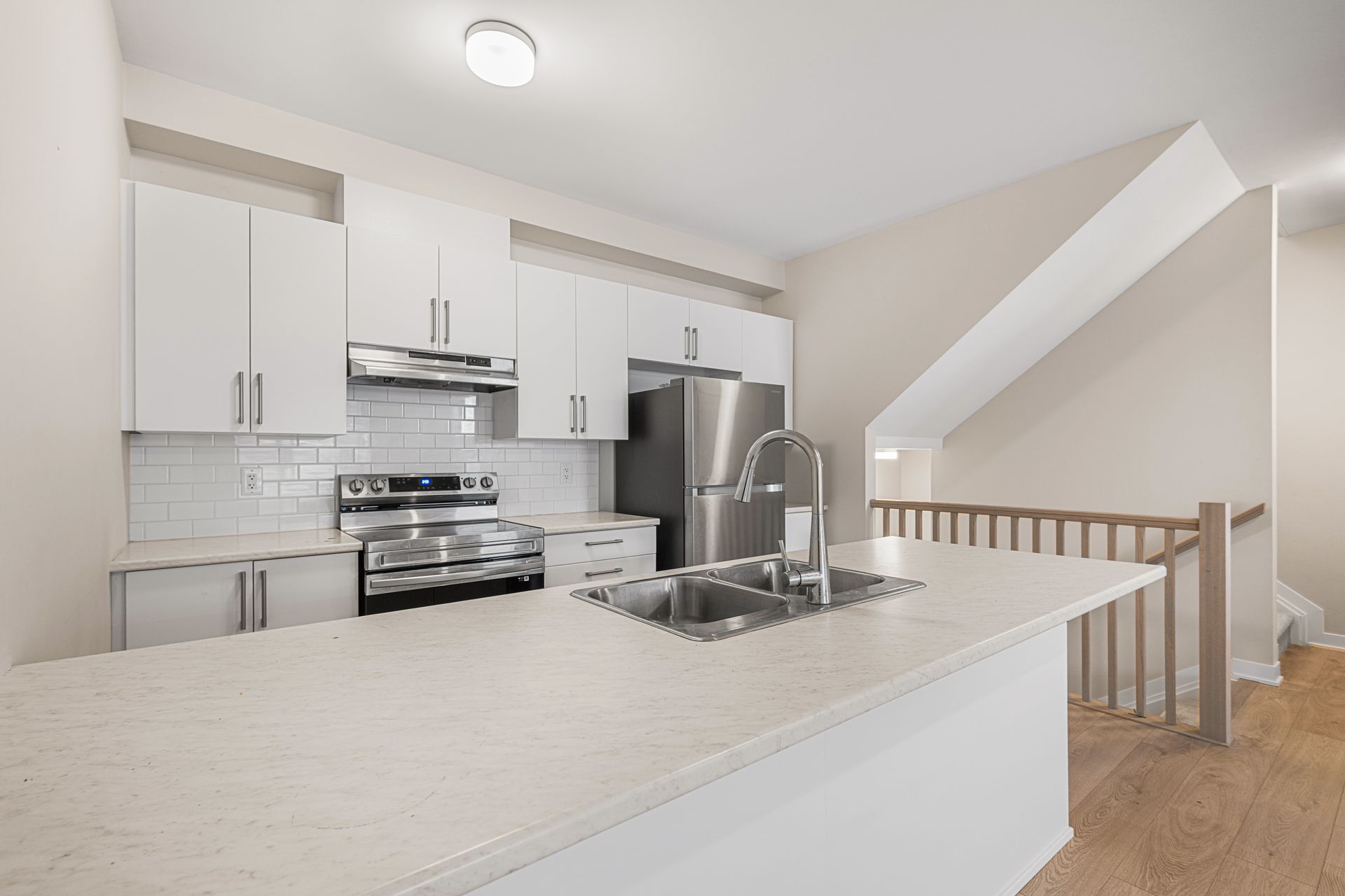 A kitchen with white cabinets , stainless steel appliances , a sink and a refrigerator.