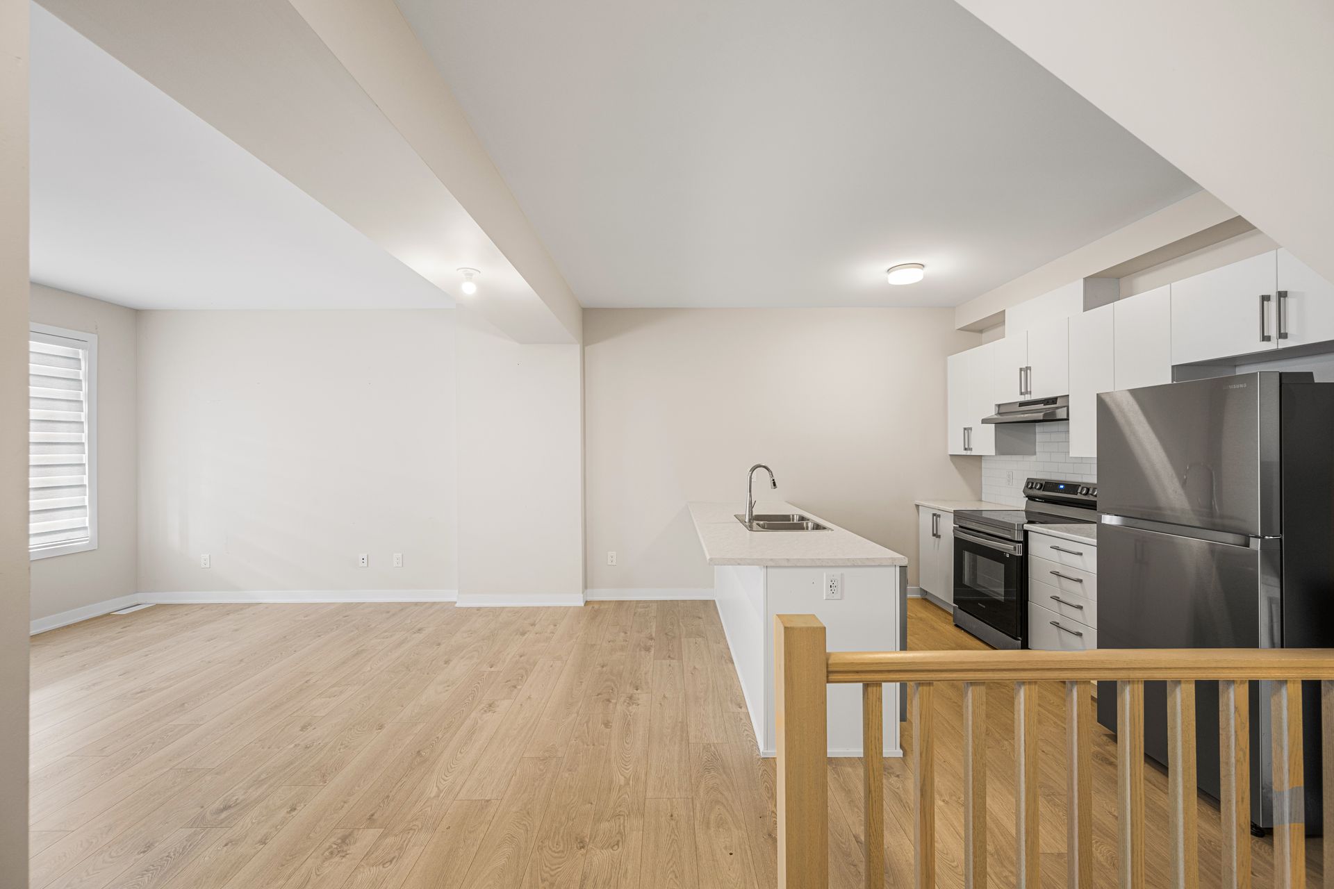 An empty kitchen with stainless steel appliances and hardwood floors.