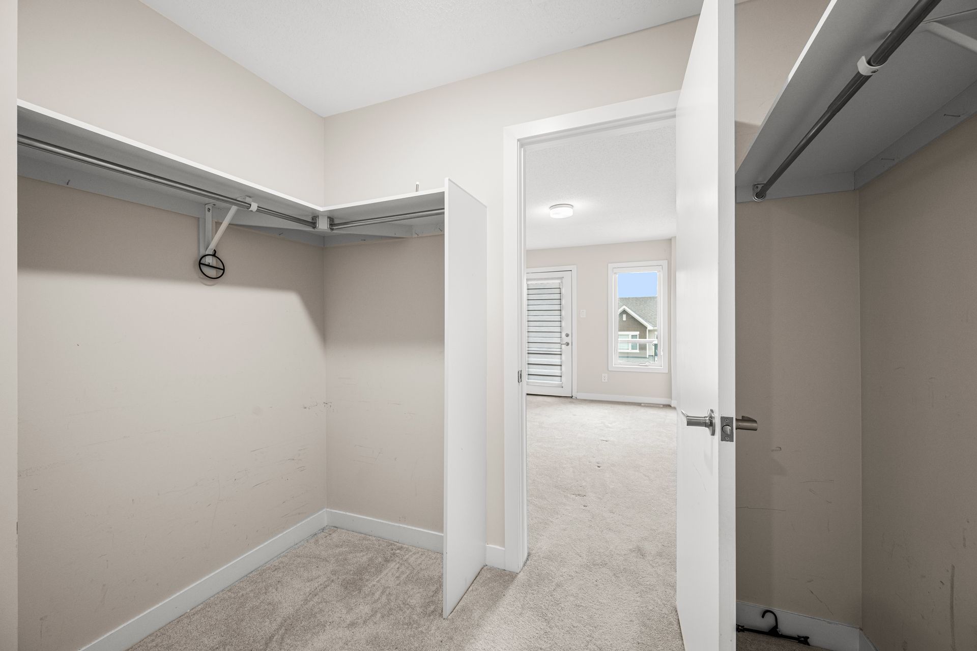 An empty walk in closet in a house with a door open leading to a bedroom.