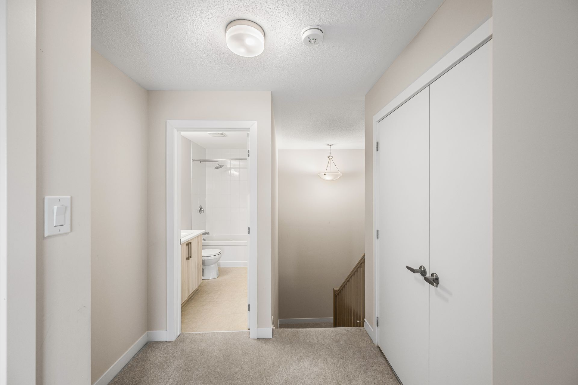 A hallway leading to a bathroom and stairs in a house.