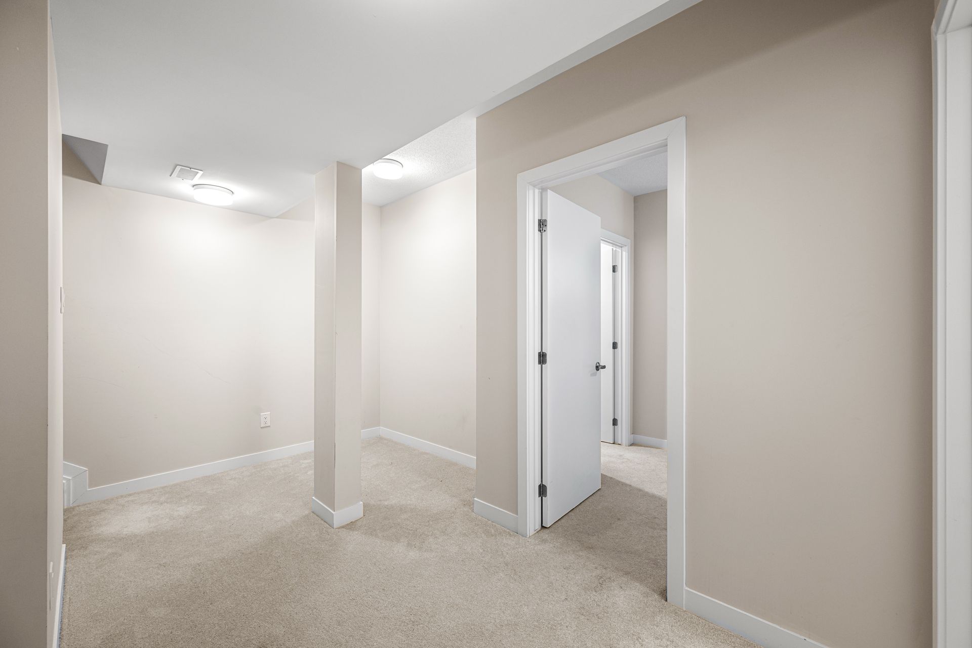 An empty basement with a carpeted floor and white walls.