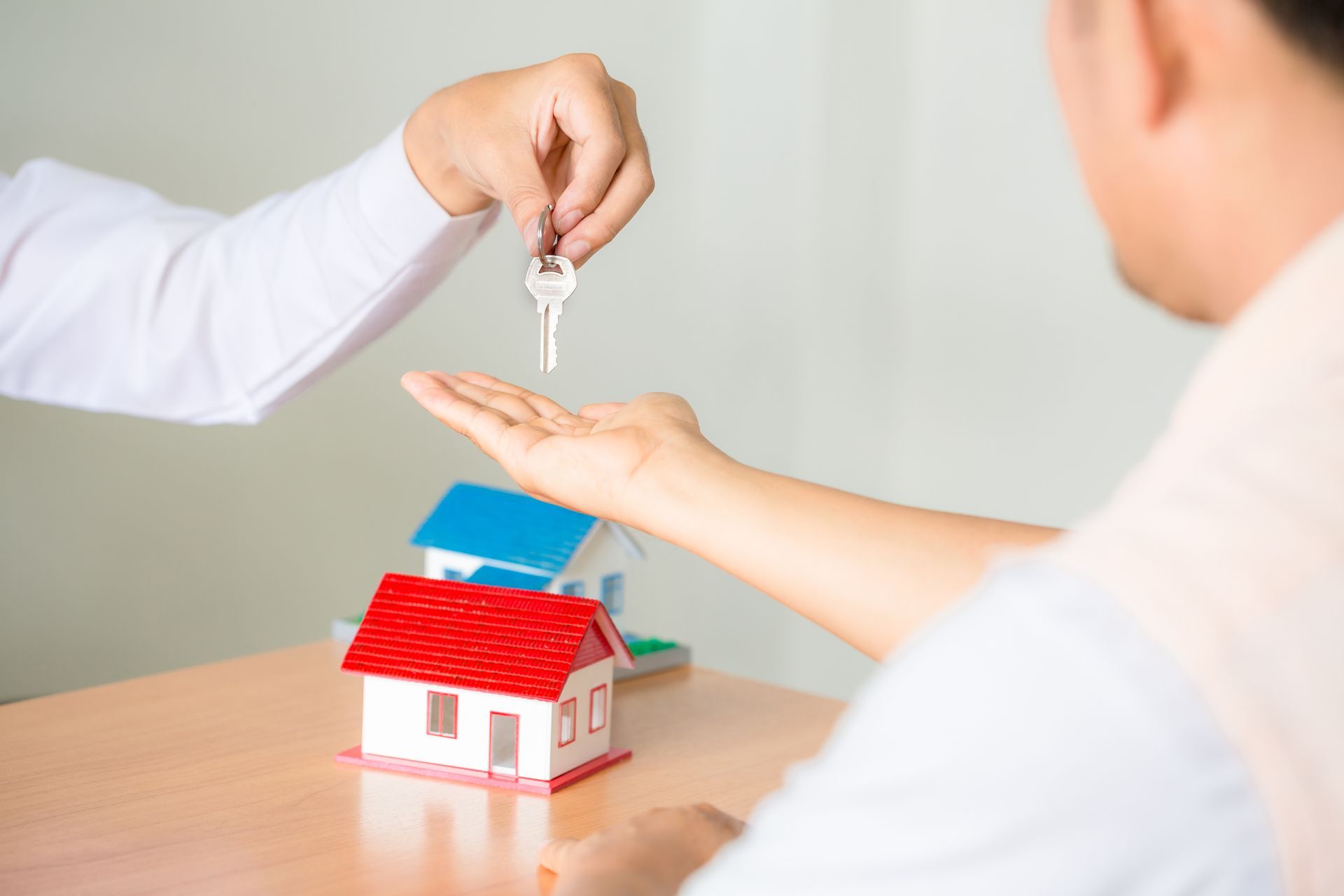 Person handing keys to another person, miniature house models on the table.