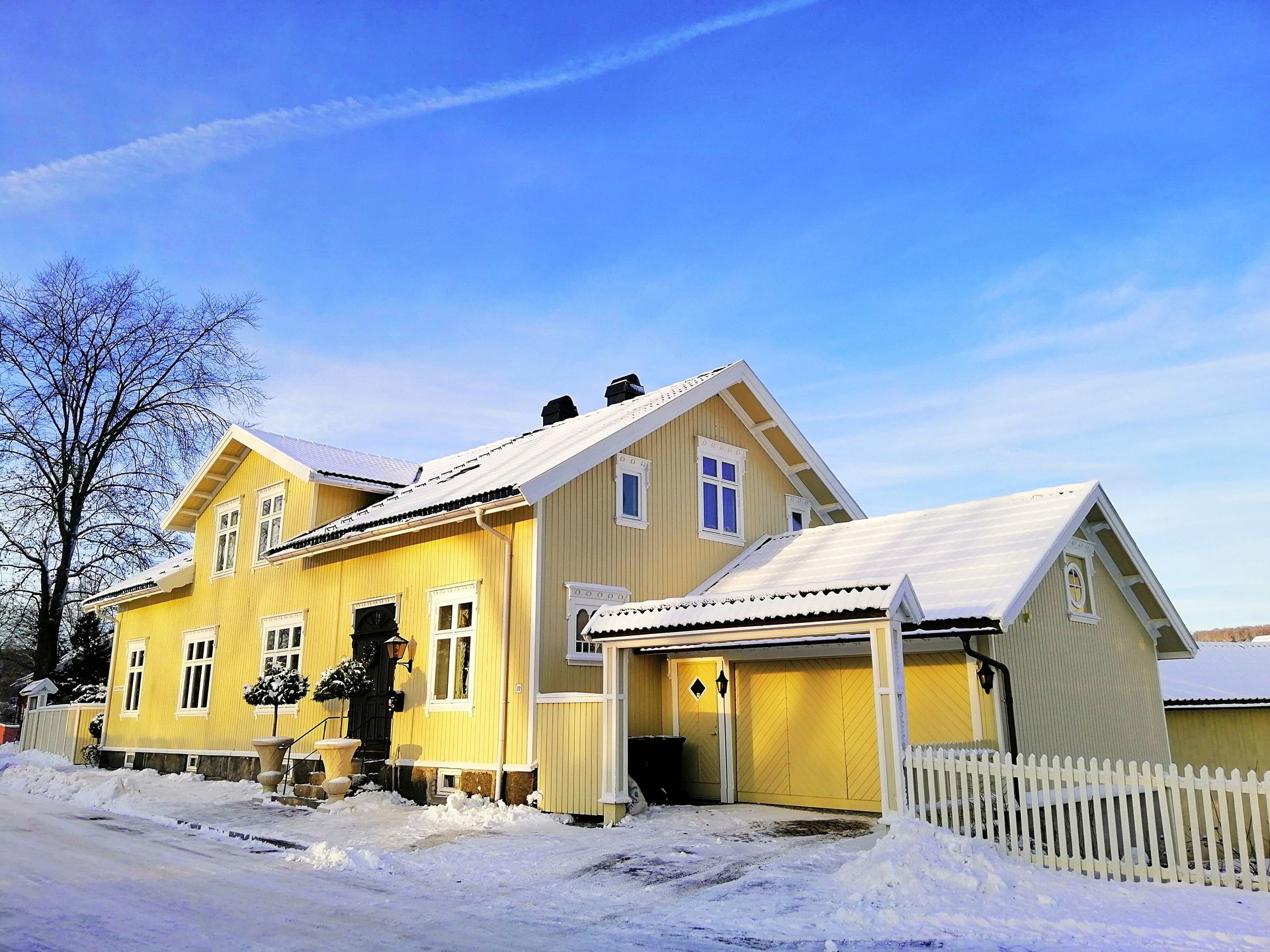 Yellow house with snow-covered roof and ground under a bright blue winter sky.