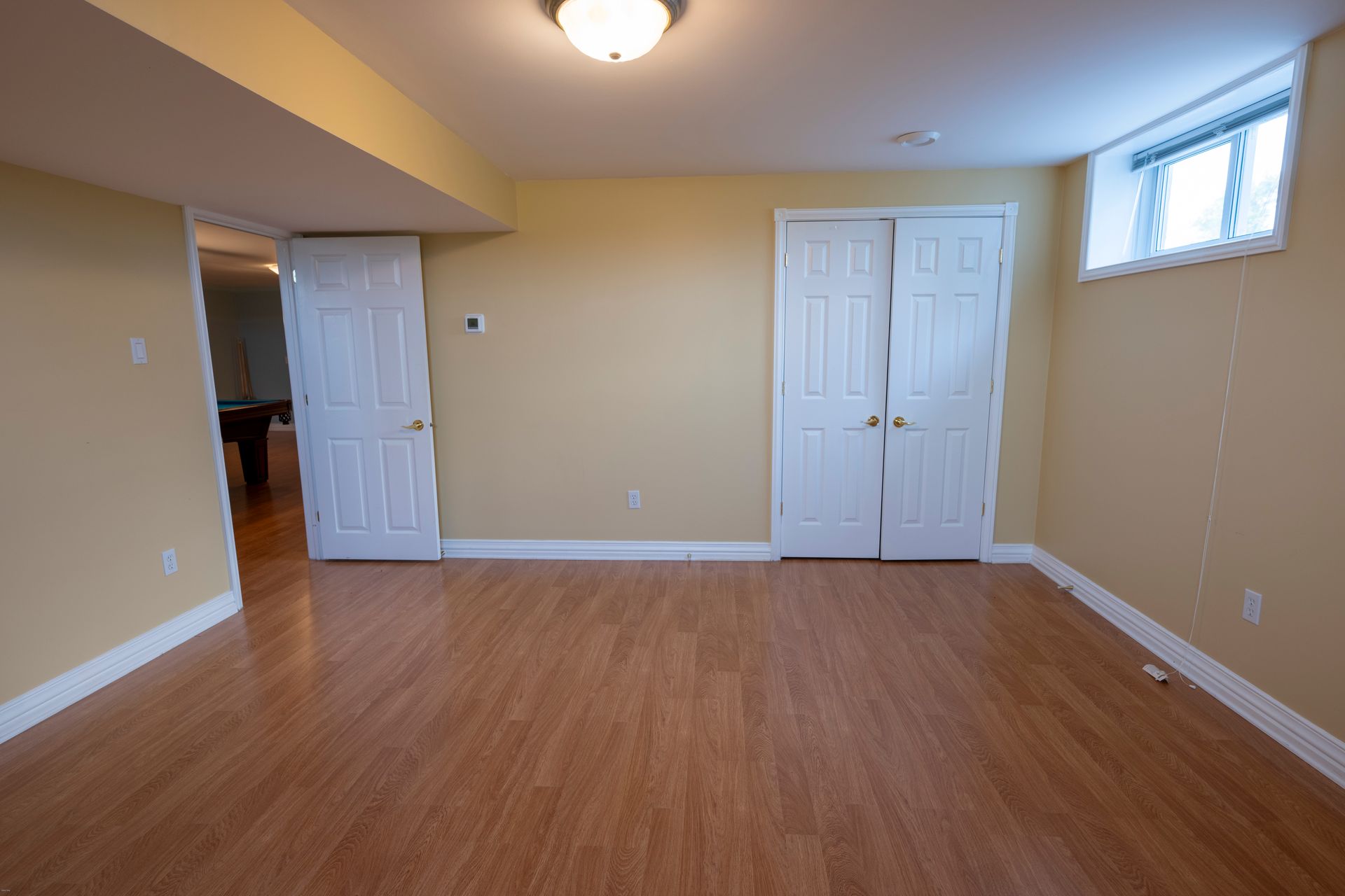 An empty basement with hardwood floors and yellow walls.