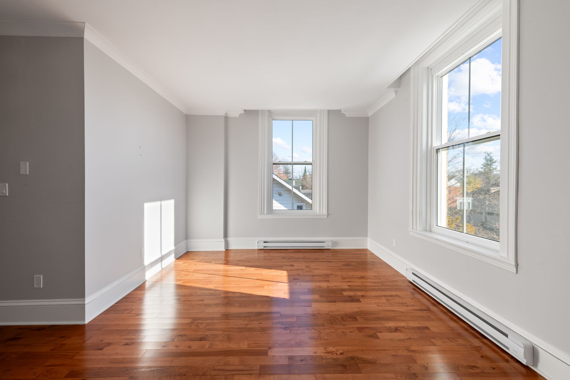 An empty room with hardwood floors and two windows