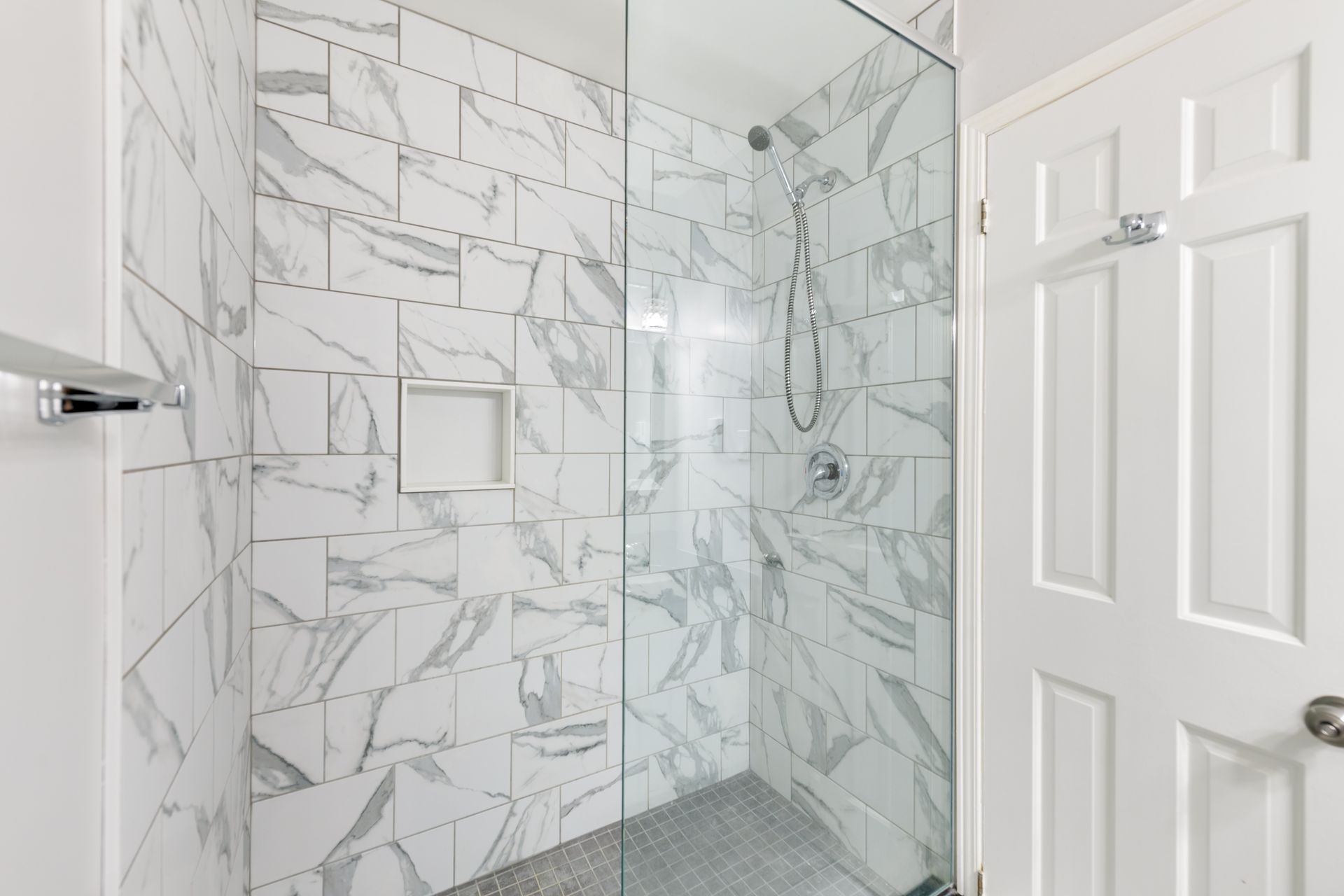 A bathroom with marble tiles and a walk in shower with a glass door.