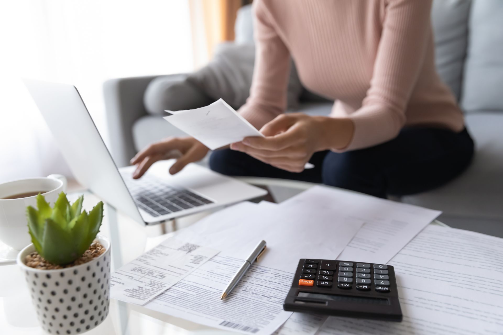 A woman is sitting on a couch using a laptop and a calculator.