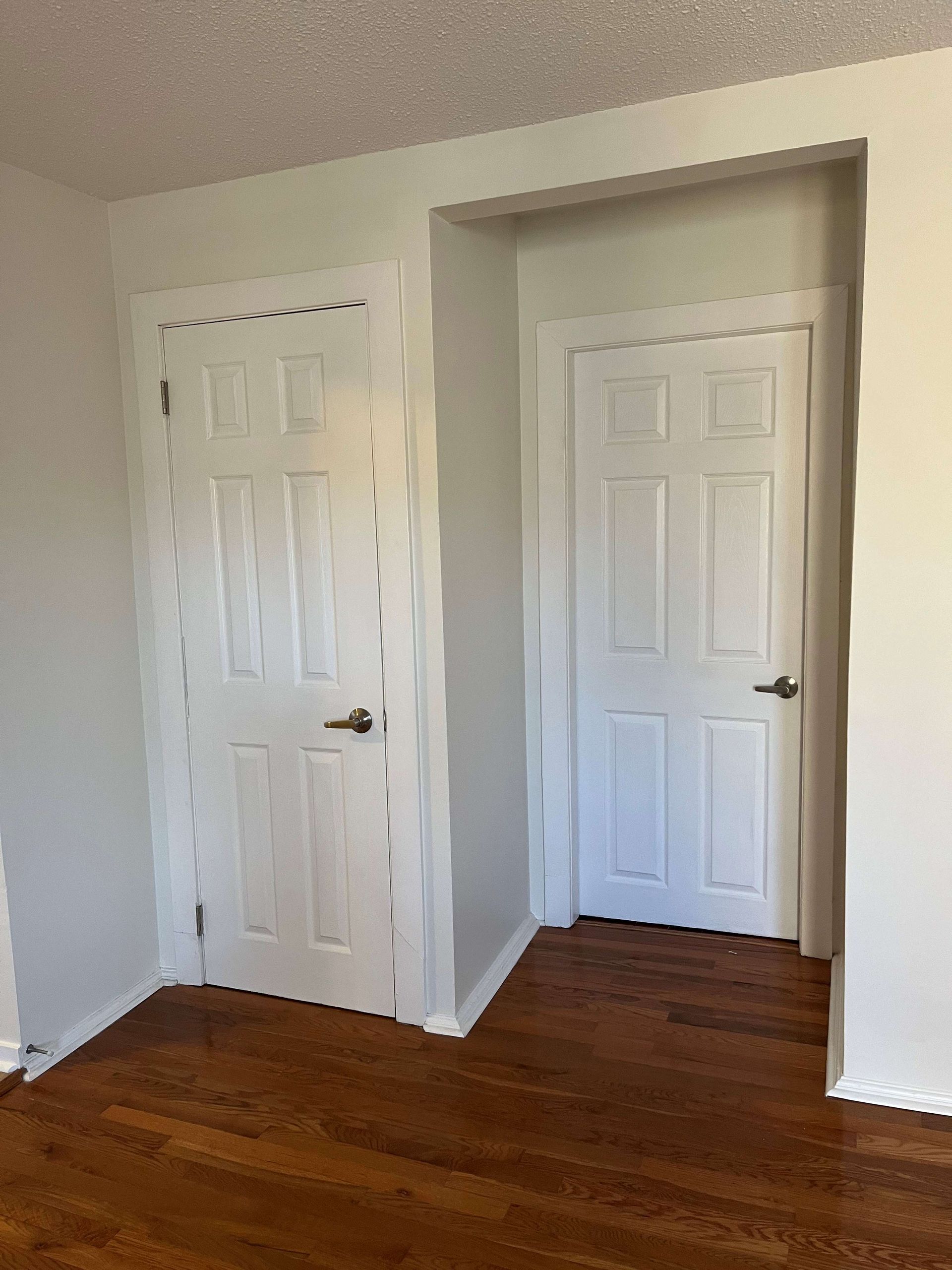 A bedroom with two white doors and hardwood floors.