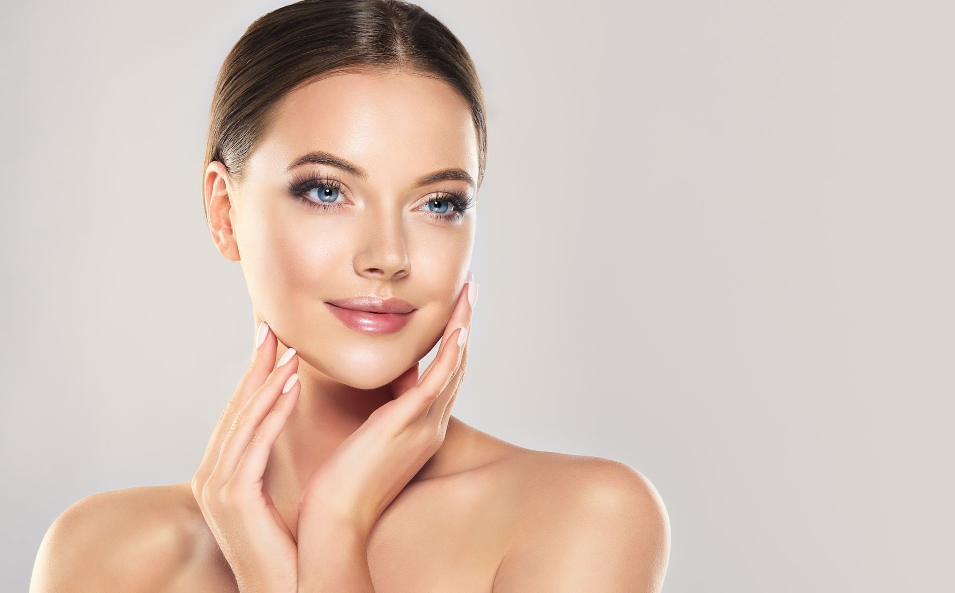 Porträt einer lächelnden Frau mit blauem Augen-Make-up, die ihre Hände am Kinn abstützt, vor einem neutralen Hintergrund