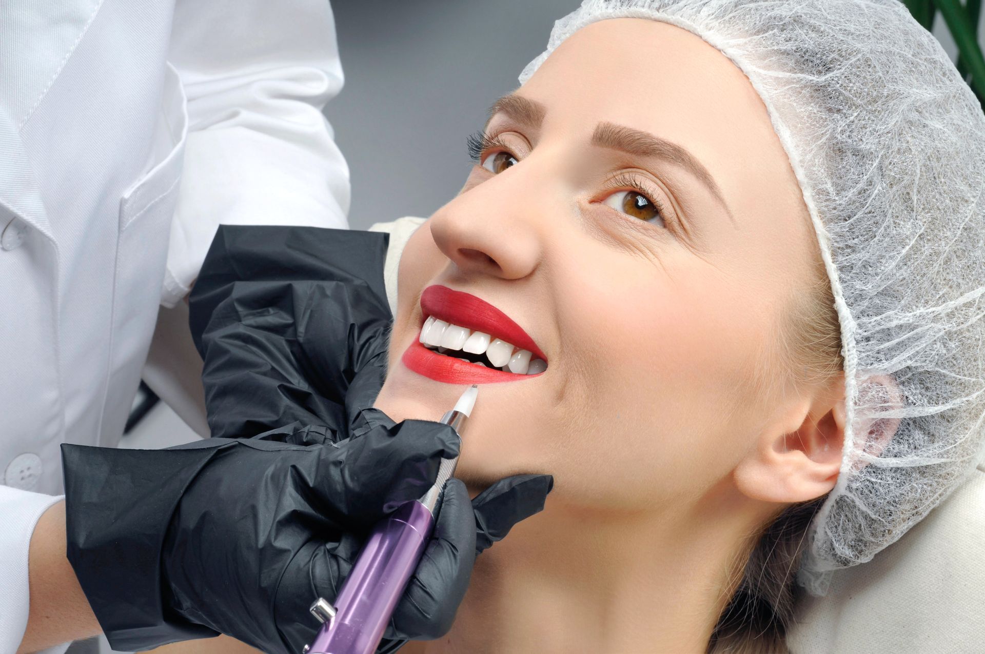 Zahnarzt führt kosmetische Behandlung an einer lächelnden Patientin mit weißen Zähnen und einer Haarkappe durch.