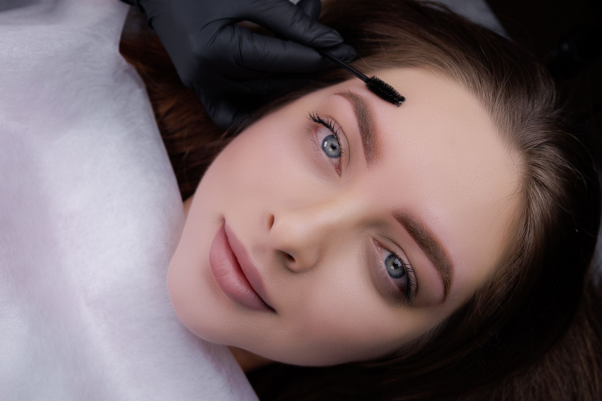 Nahaufnahme einer Frau, die auf einem Kissen liegt, während eine behandschuhte Hand ihre Stirn berührt.