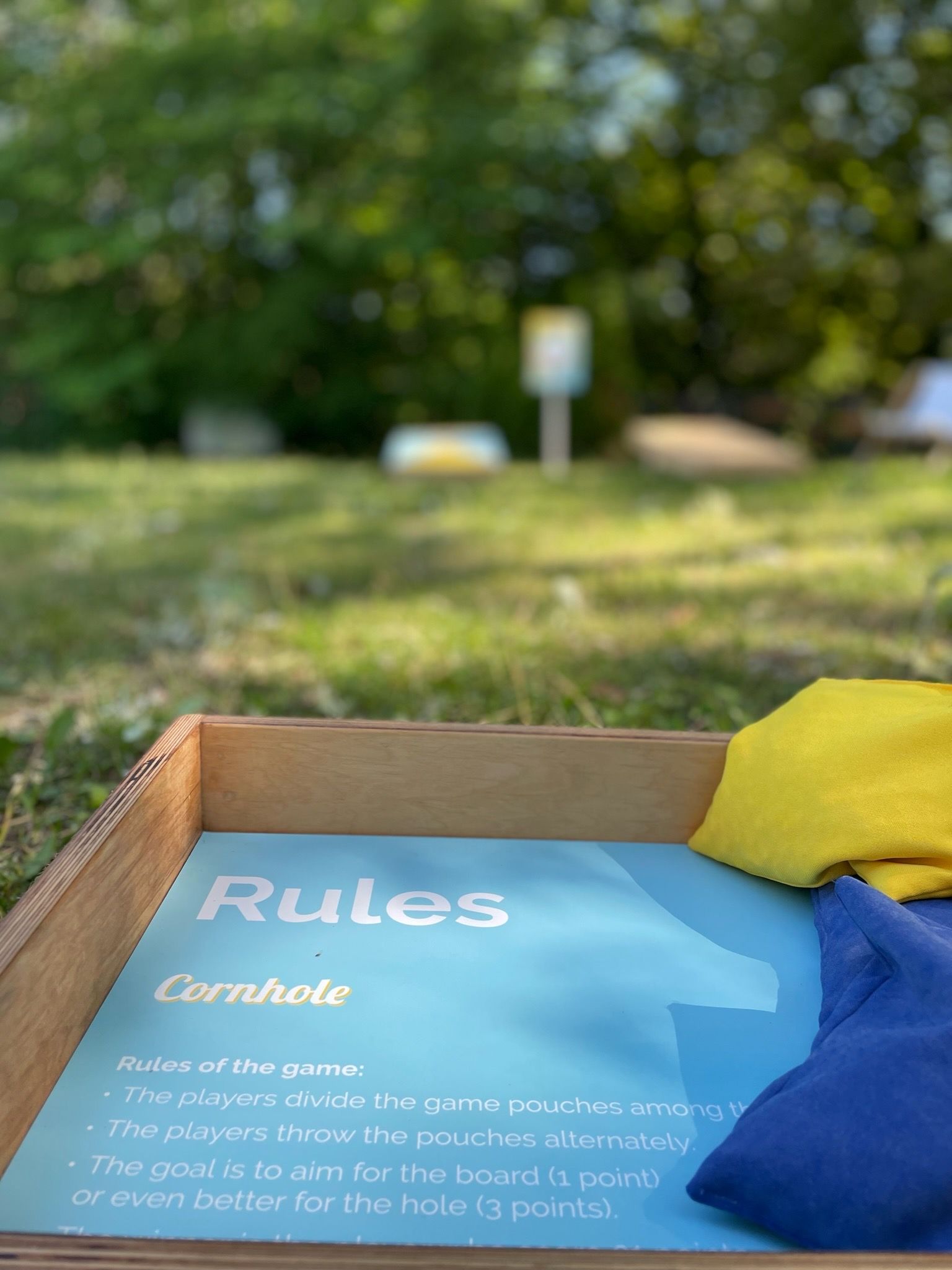 drewniane pudełko wypełnione workami z dziurami i tabliczką z napisem „Zasady”.