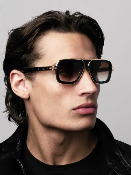 Man wearing dark sunglasses with gold accents, looking slightly away.