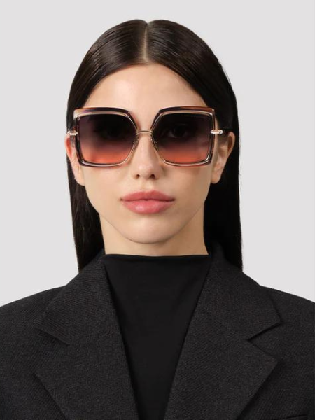 Woman wearing oversized square sunglasses with ombre lenses, black blazer.